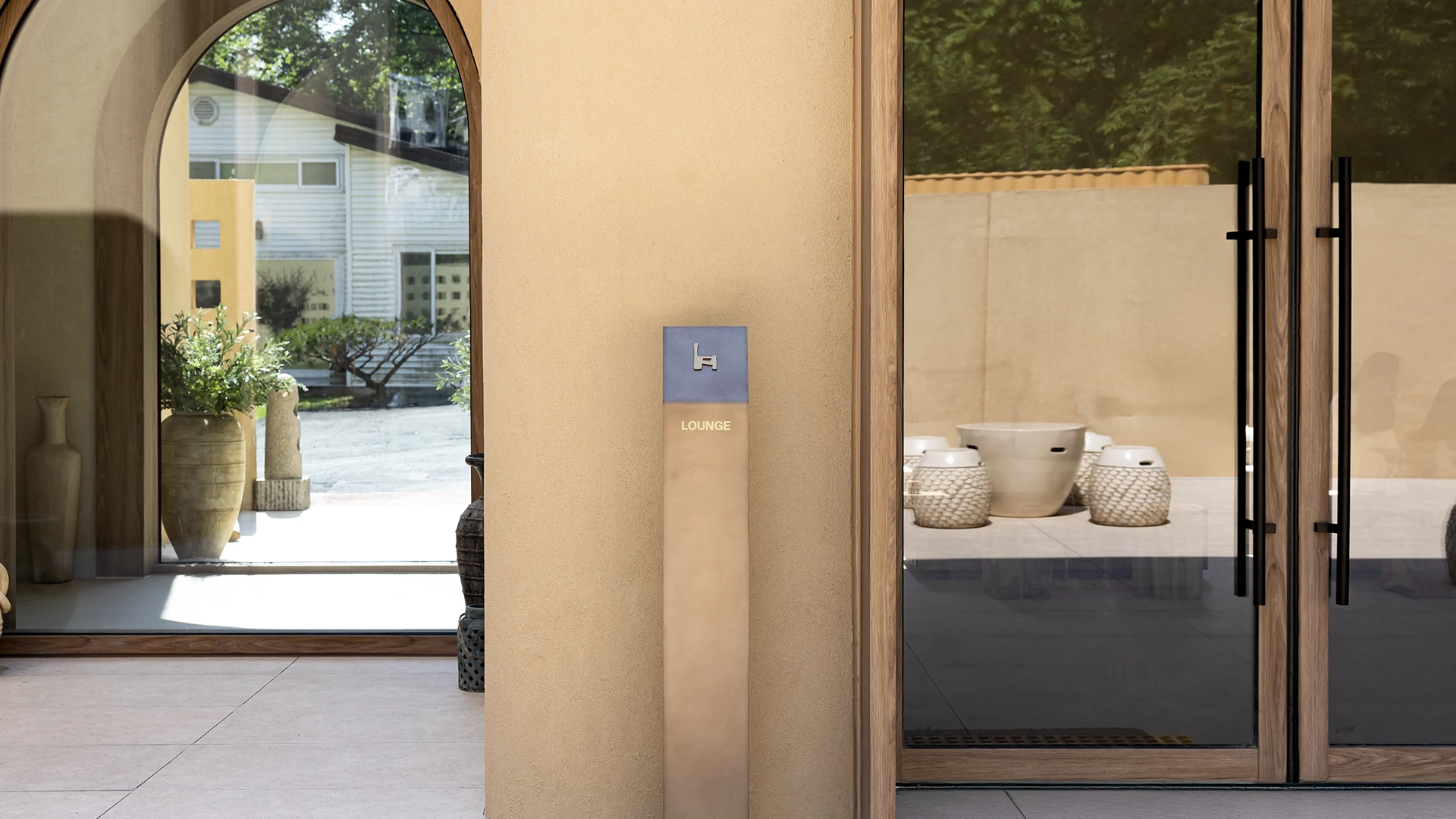 Entrance to MAZIMOU with a curved archway and glass double doors, showing a 'LOUNGE' sign and outdoor patio with white planters.