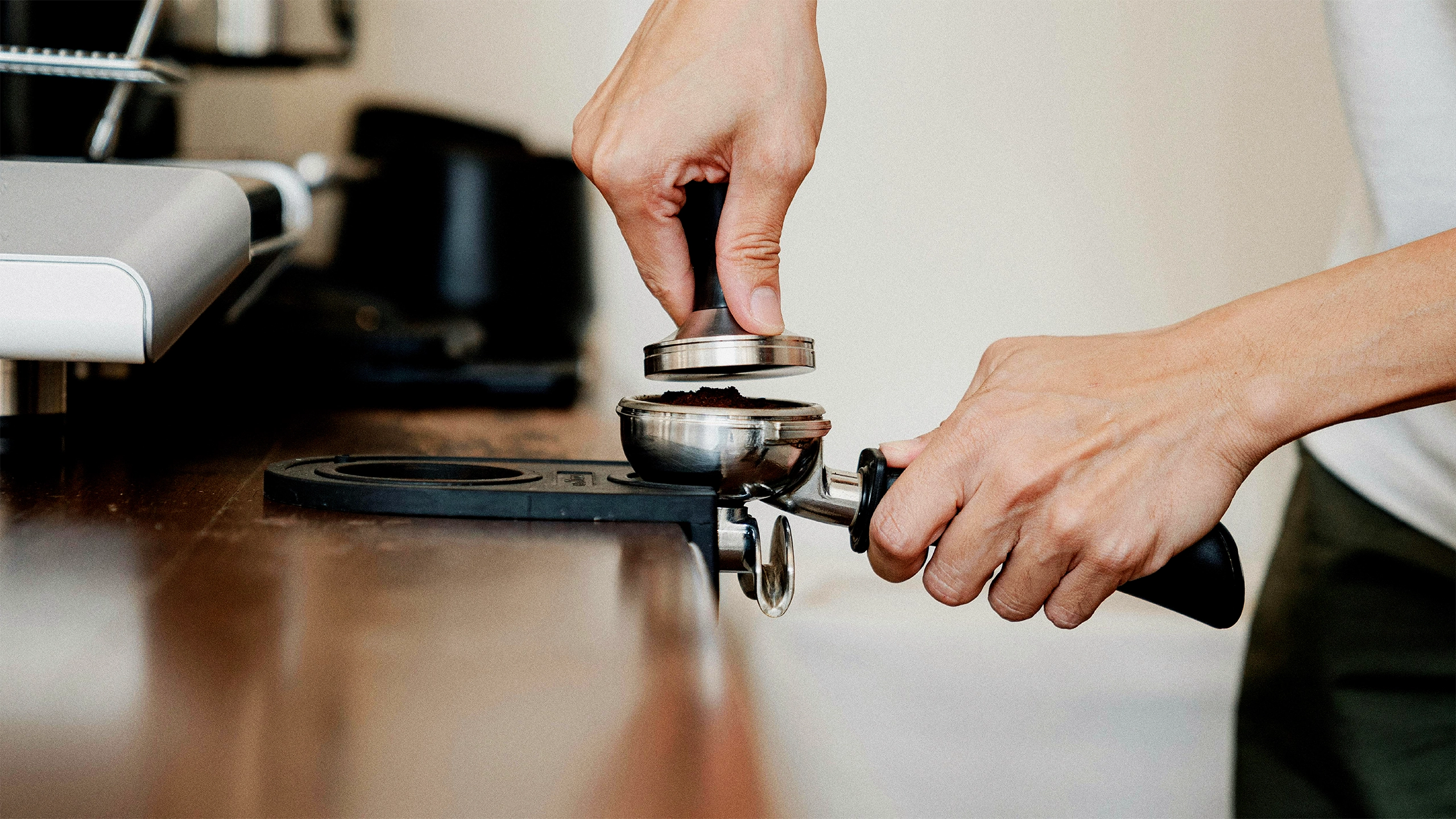 Close-up of hands tamping coffee grounds in a portafilter, preparing espresso