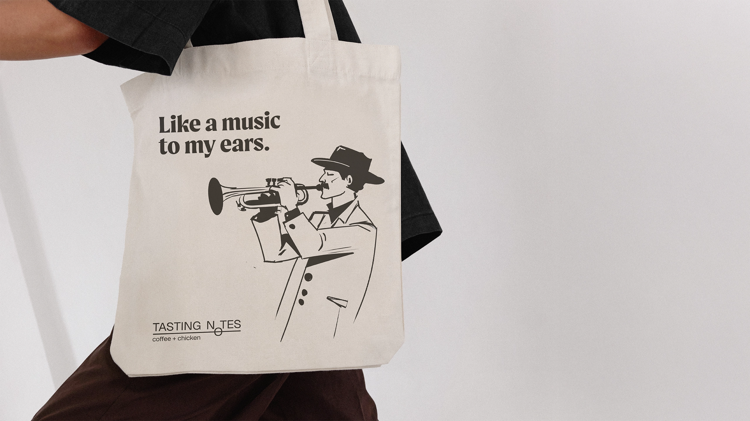 Person carrying a canvas tote bag with a jazz musician illustration and 'Tasting Notes coffee + chicken' logo