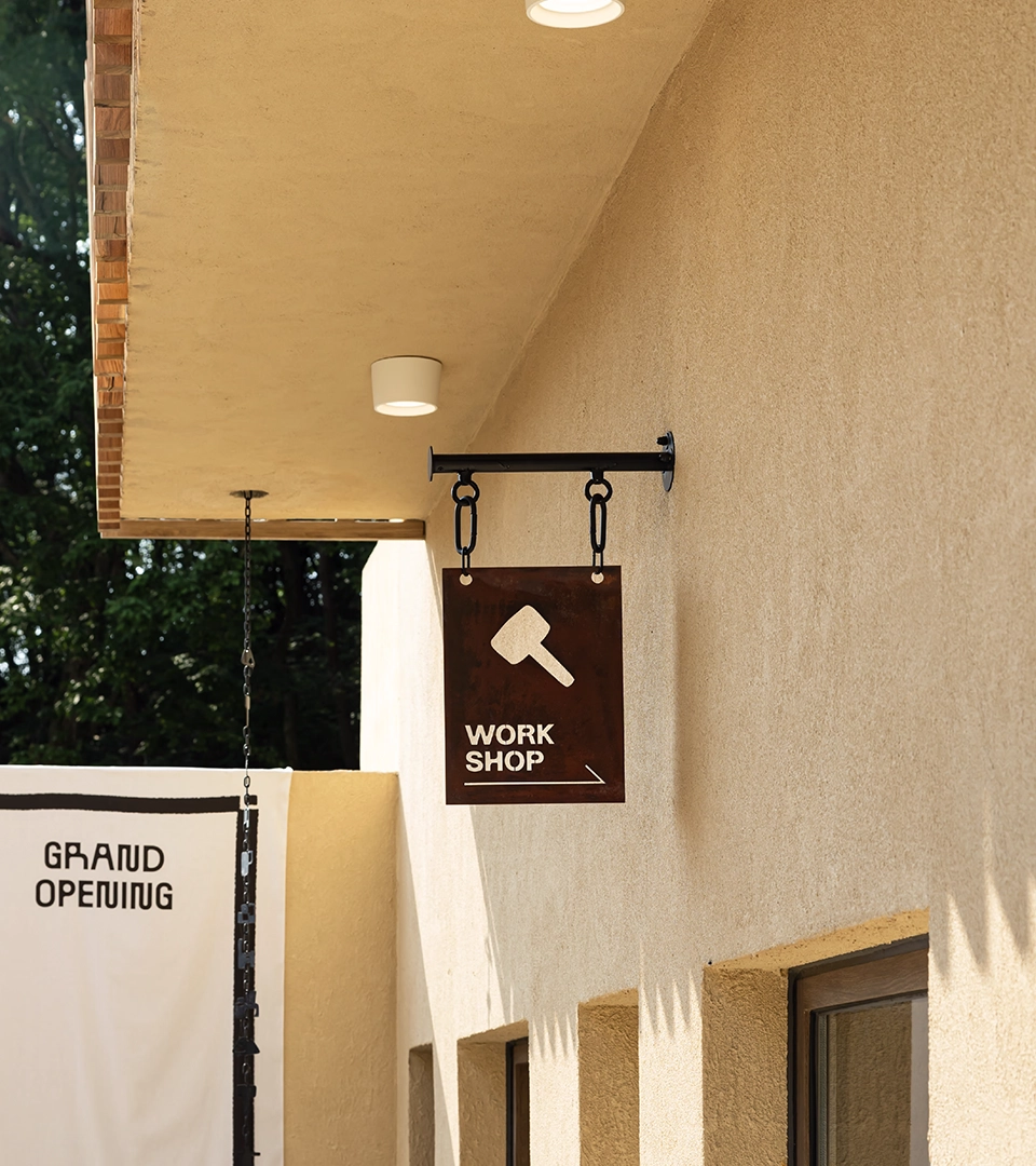 Exterior view of MAZIMOU building with a 'WORKSHOP' sign featuring a hammer icon and a 'GRAND OPENING' banner.