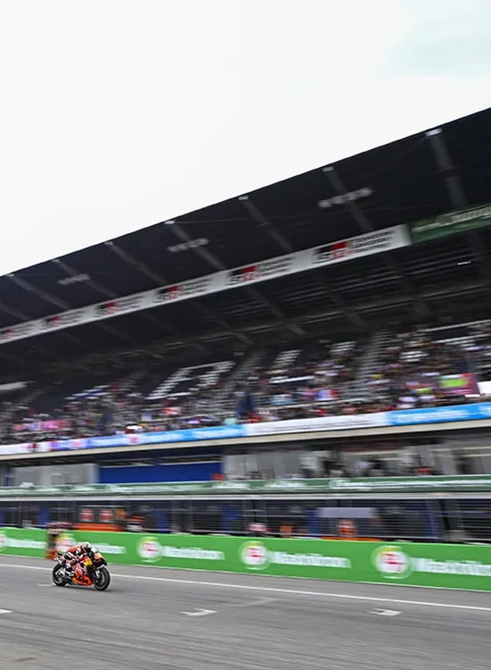 Pedro Acosta speeds along a track with a grandstand full of spectators in the background.