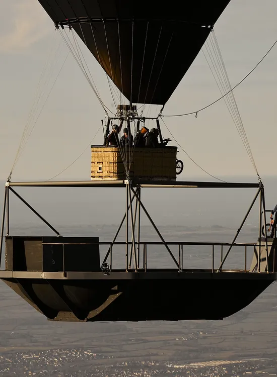 Hot air balloon in the sky with Kris Kyle poised on a platform edge, framed by expansive landscape below.