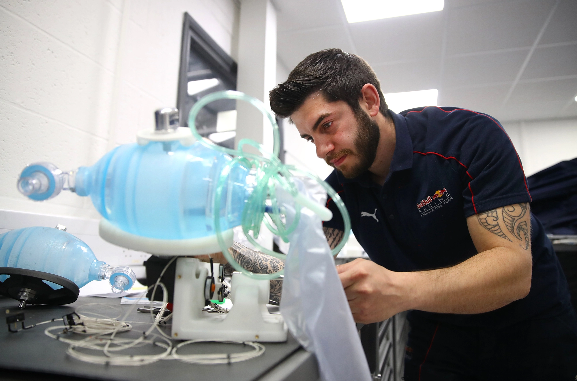 A man in a navy shirt examines a blue medical device with tubes and wires in a lab setting.
