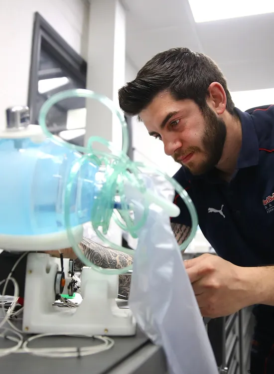 A man in a navy shirt examines a blue medical device with tubes and wires in a lab setting.