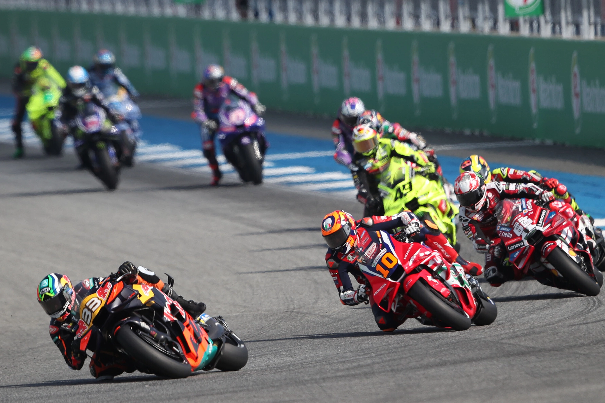 Motorcycle racers lean sharply during a high-speed race, competing closely on a track.