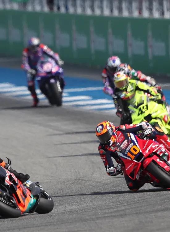 Motorcycle racers lean sharply during a high-speed race, competing closely on a track.