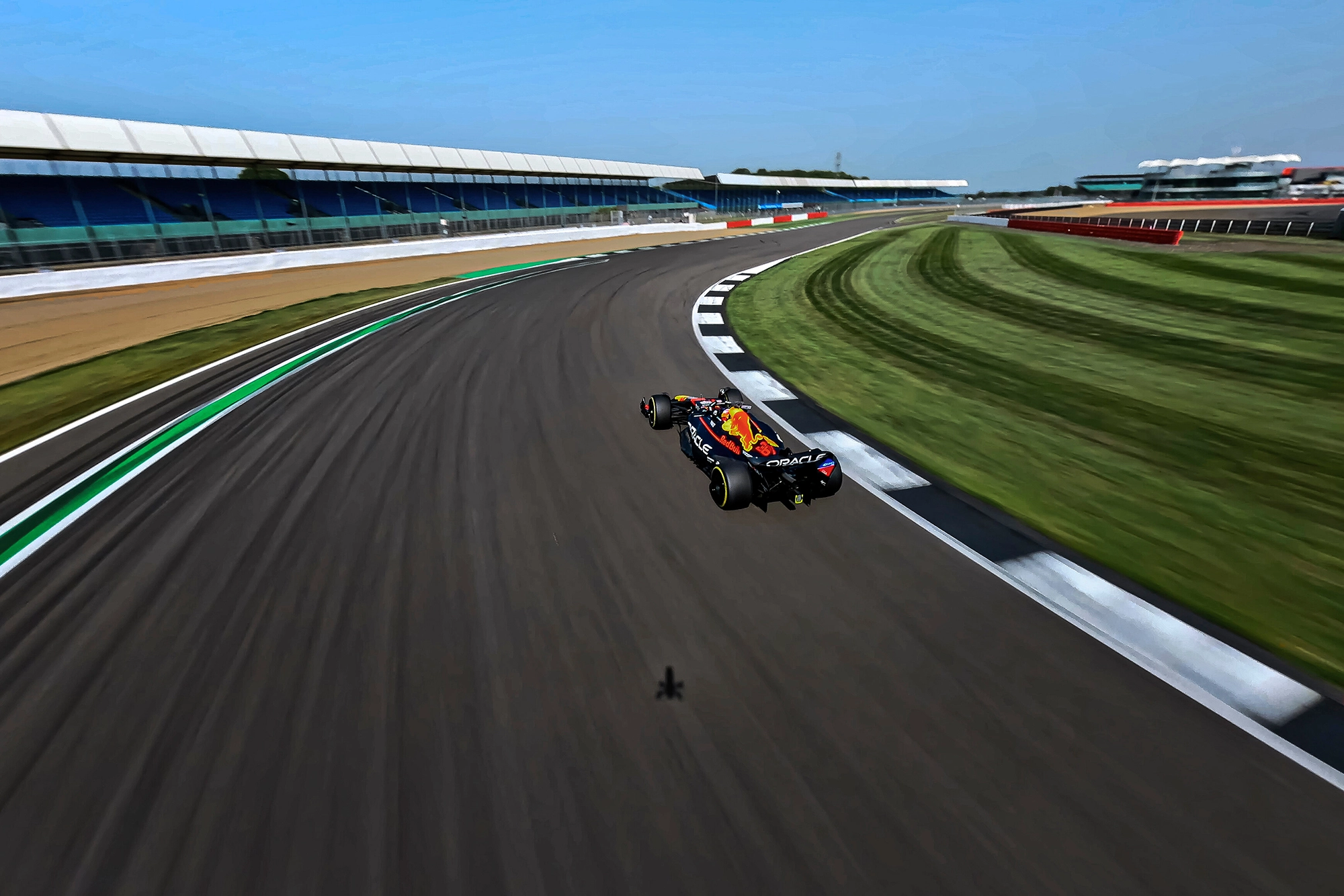 An F1 car racing on a curving track at a motorsport circuit, surrounded by green grass and clear blue sky.
