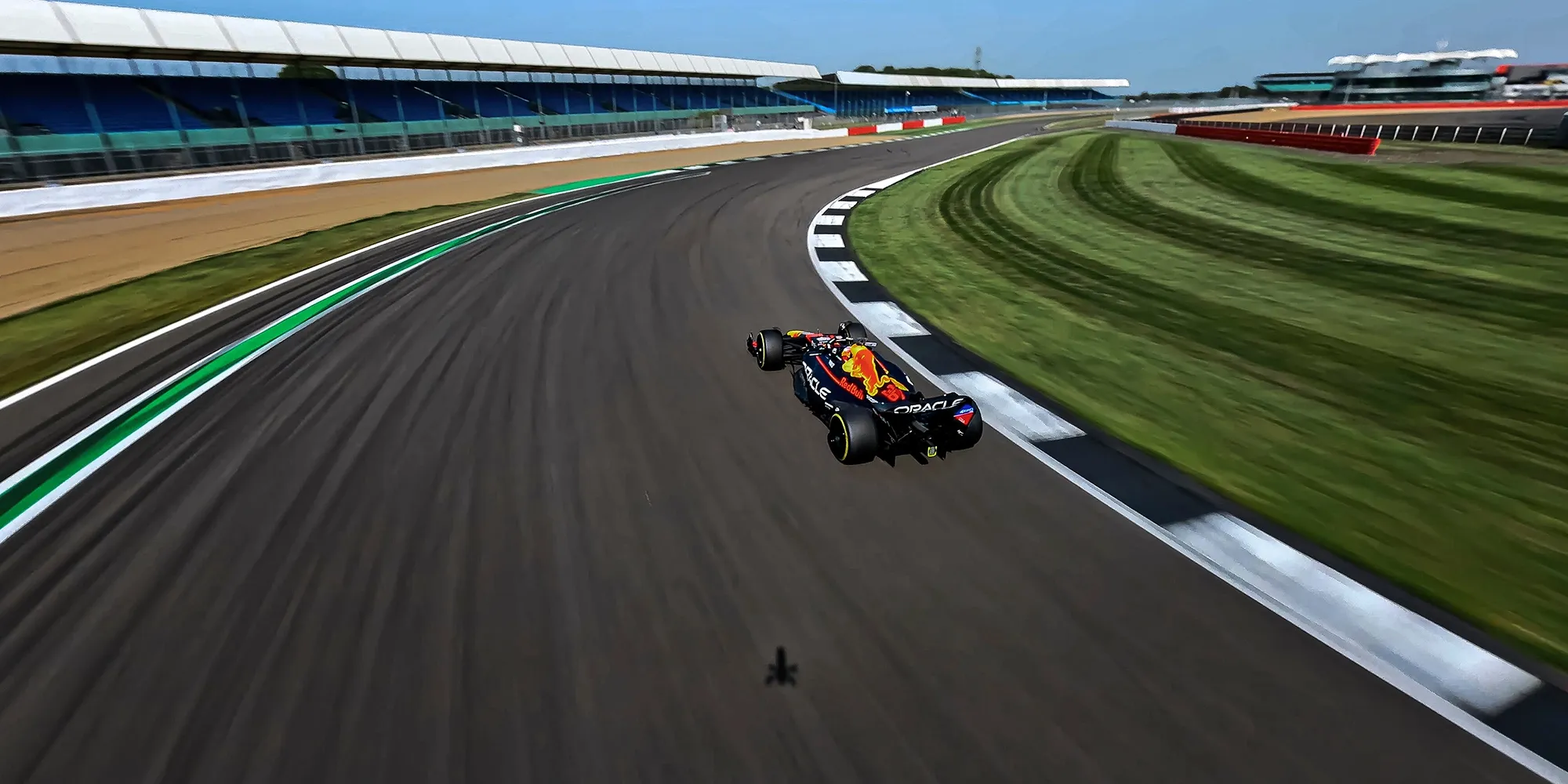 An F1 car racing on a curving track at a motorsport circuit, surrounded by green grass and clear blue sky.