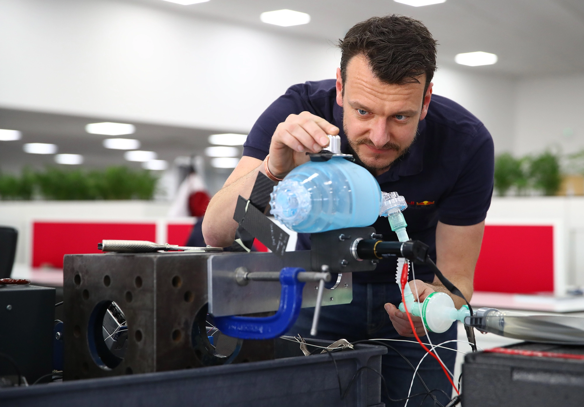 A man inspects a blue medical device in an office setting, focusing intently on its components.