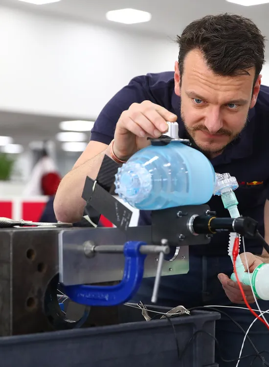 A man inspects a blue medical device in an office setting, focusing intently on its components.