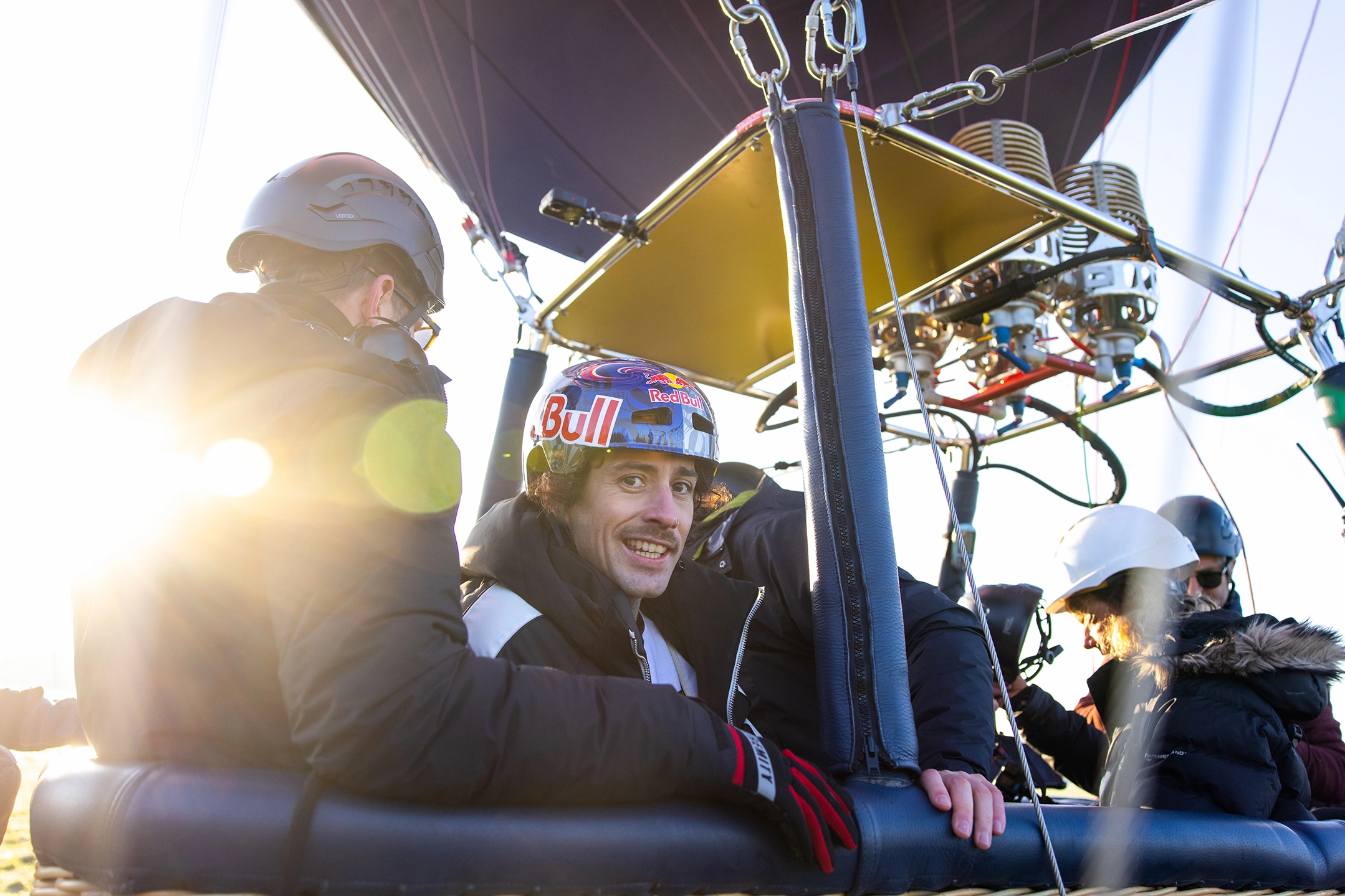 Kris Kyle with crew in a hot air balloon basket, wearing helmets and gear, with bright sunlight in the background.