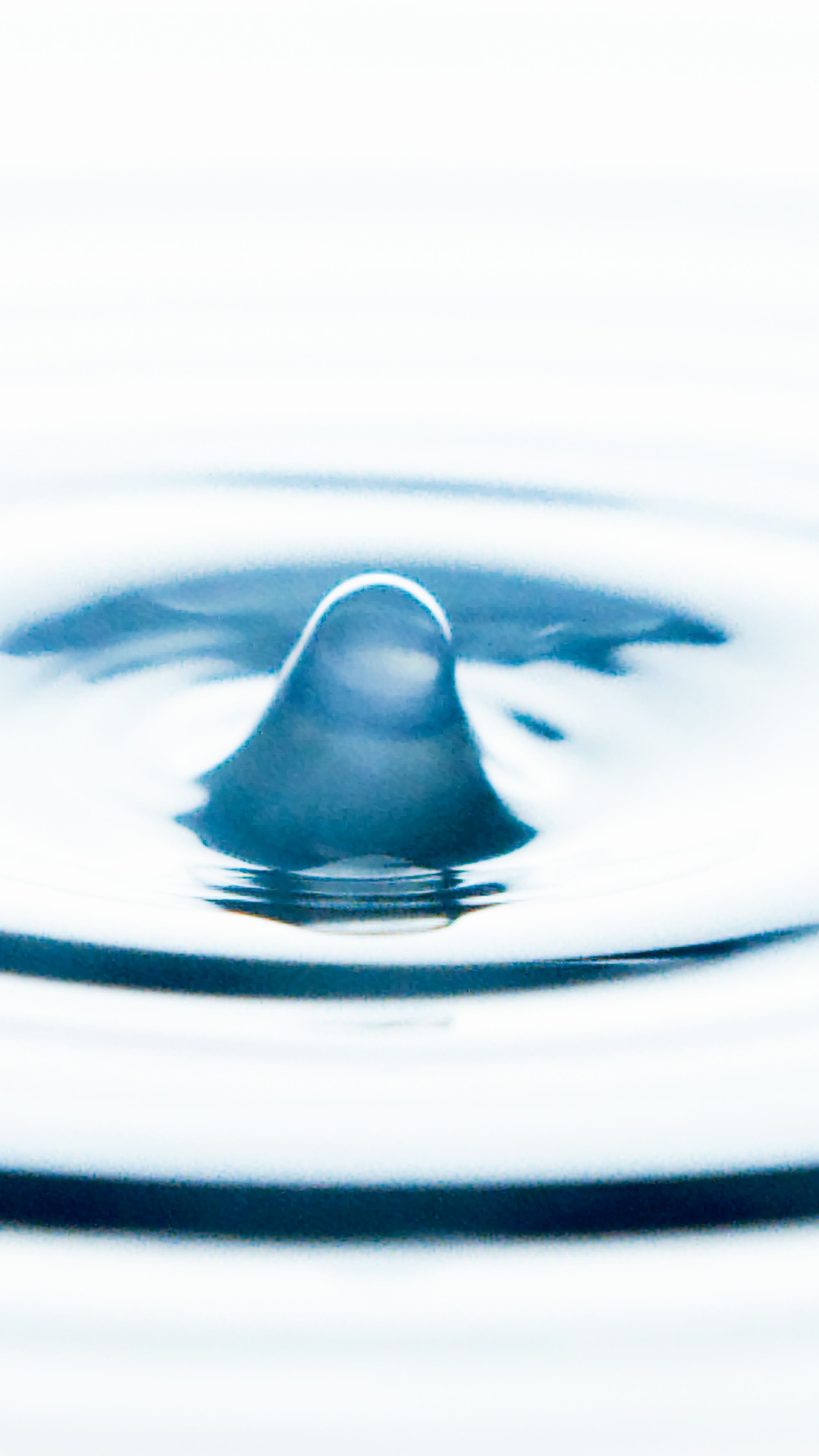 Close-up of a water droplet creating ripples on a smooth blue surface.