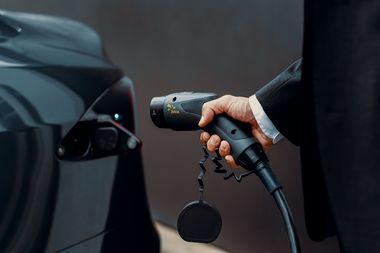 Ein Mensch steckt ein Ladekabel in ein Elektroauto