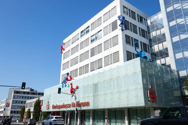 Das Gebäude der Kreissparkasse Heilbronn von der Straße aus gesehen. Bunte installierte Kunstfiguren klettern an der Fassade entlang.
