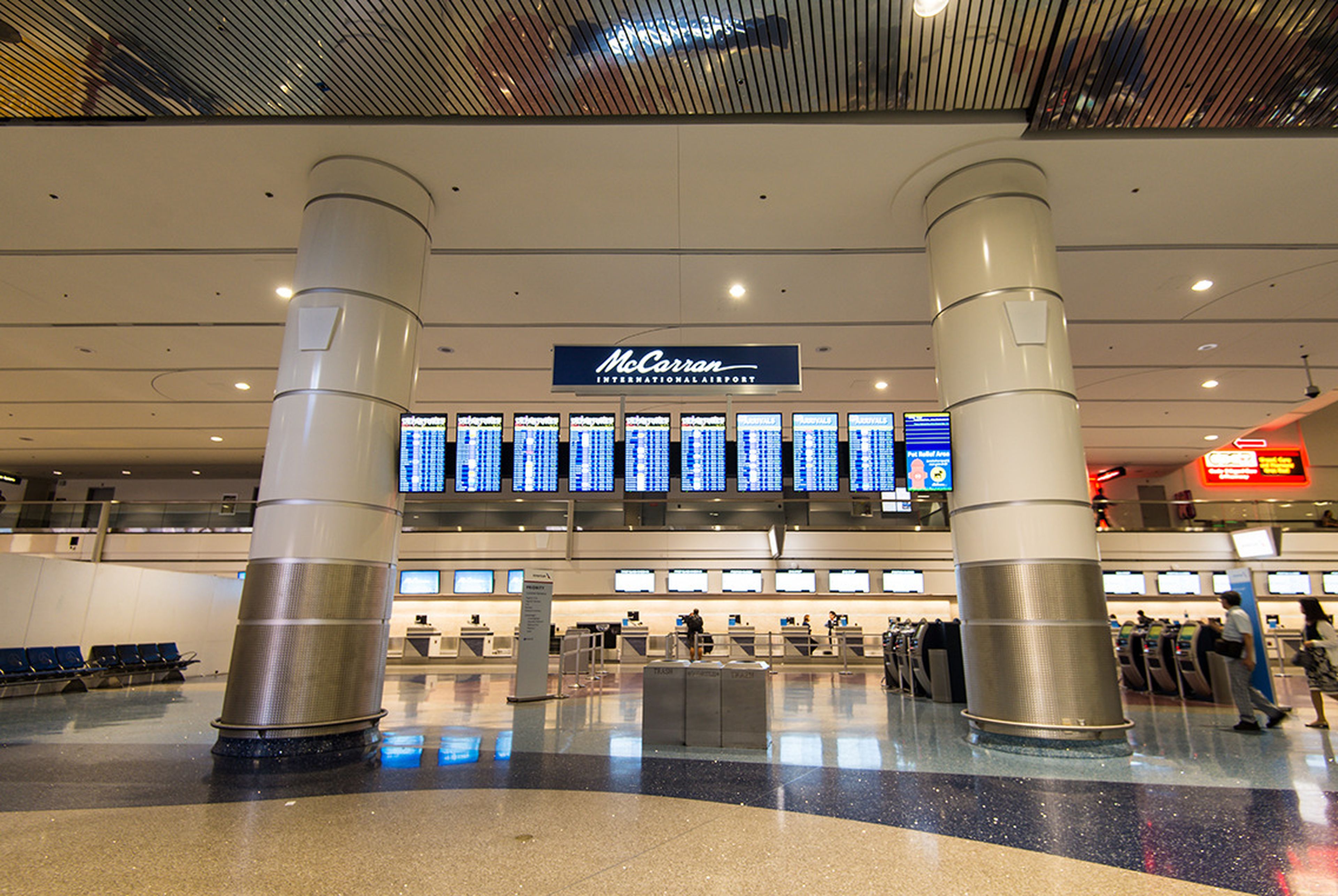 Interior of an airport terminal with flight information displays, check-in counters, and large columns. The sign reads "McCarran International Airport."