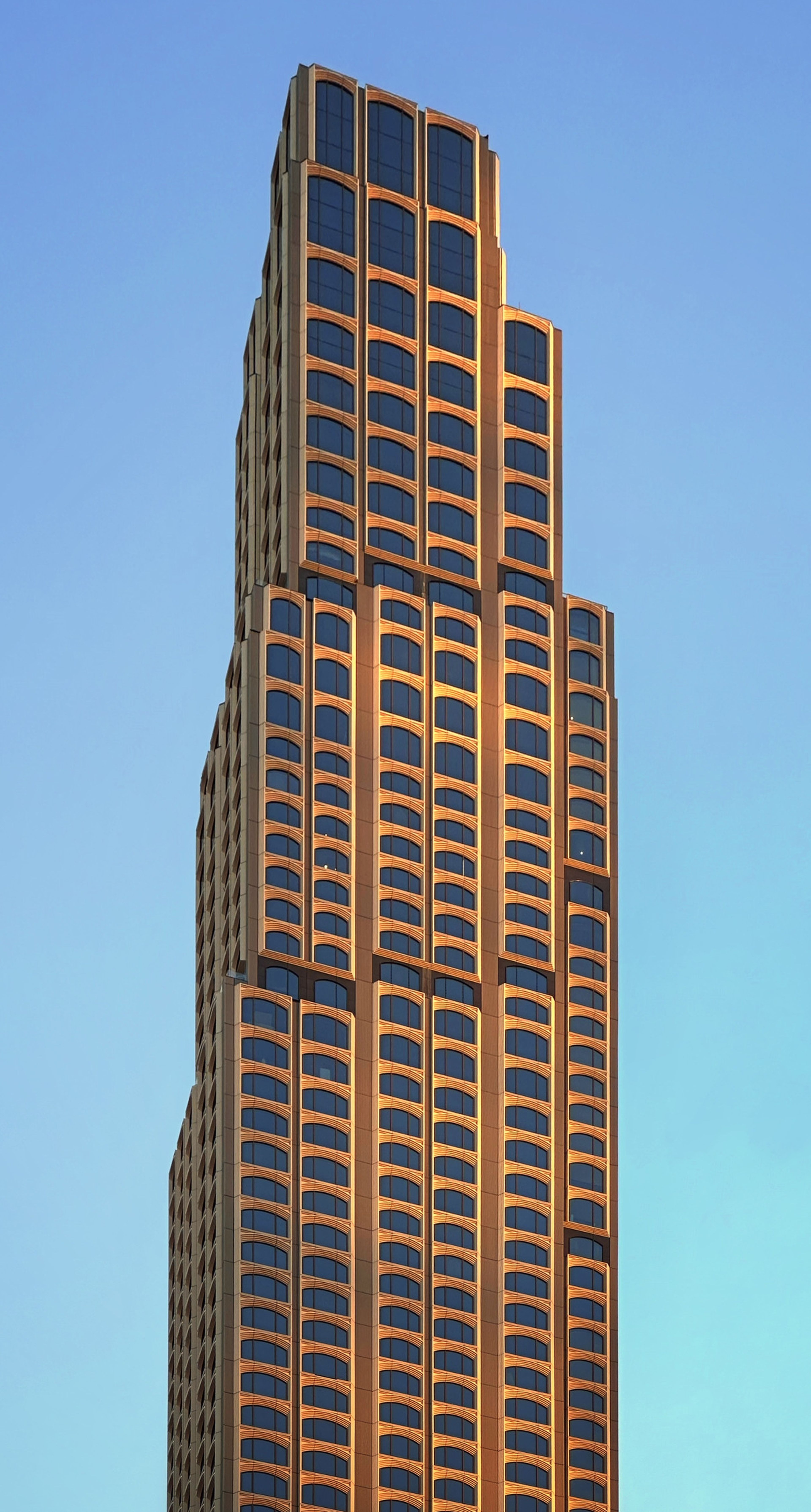 A tall, modern skyscraper with a tiered structure and numerous windows, set against a clear blue sky.