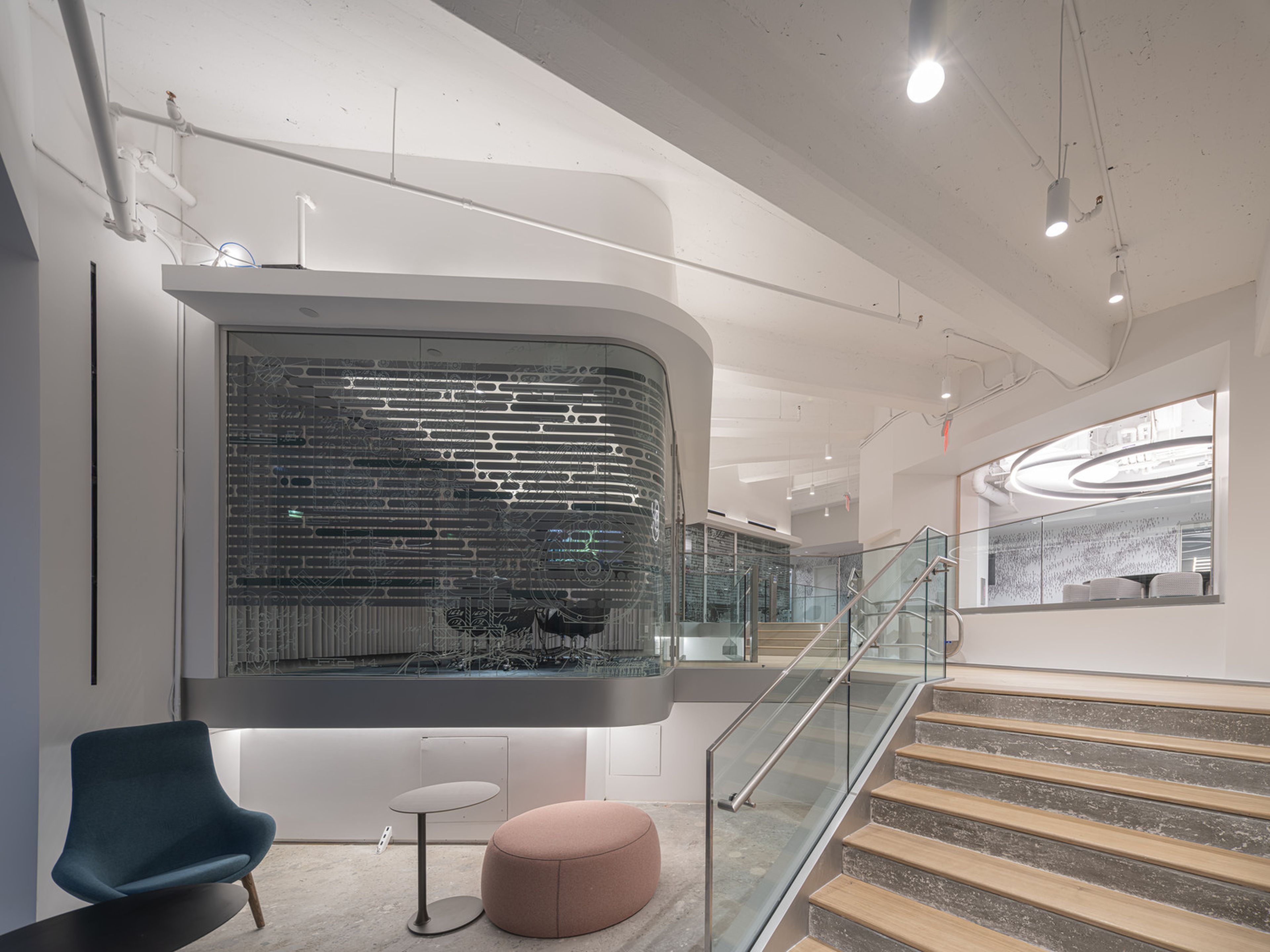 Modern, multi-level conference center with sleek bright design, featuring a curved fritted glass wall, staircase, teal chair, round table, and pink ottoman.