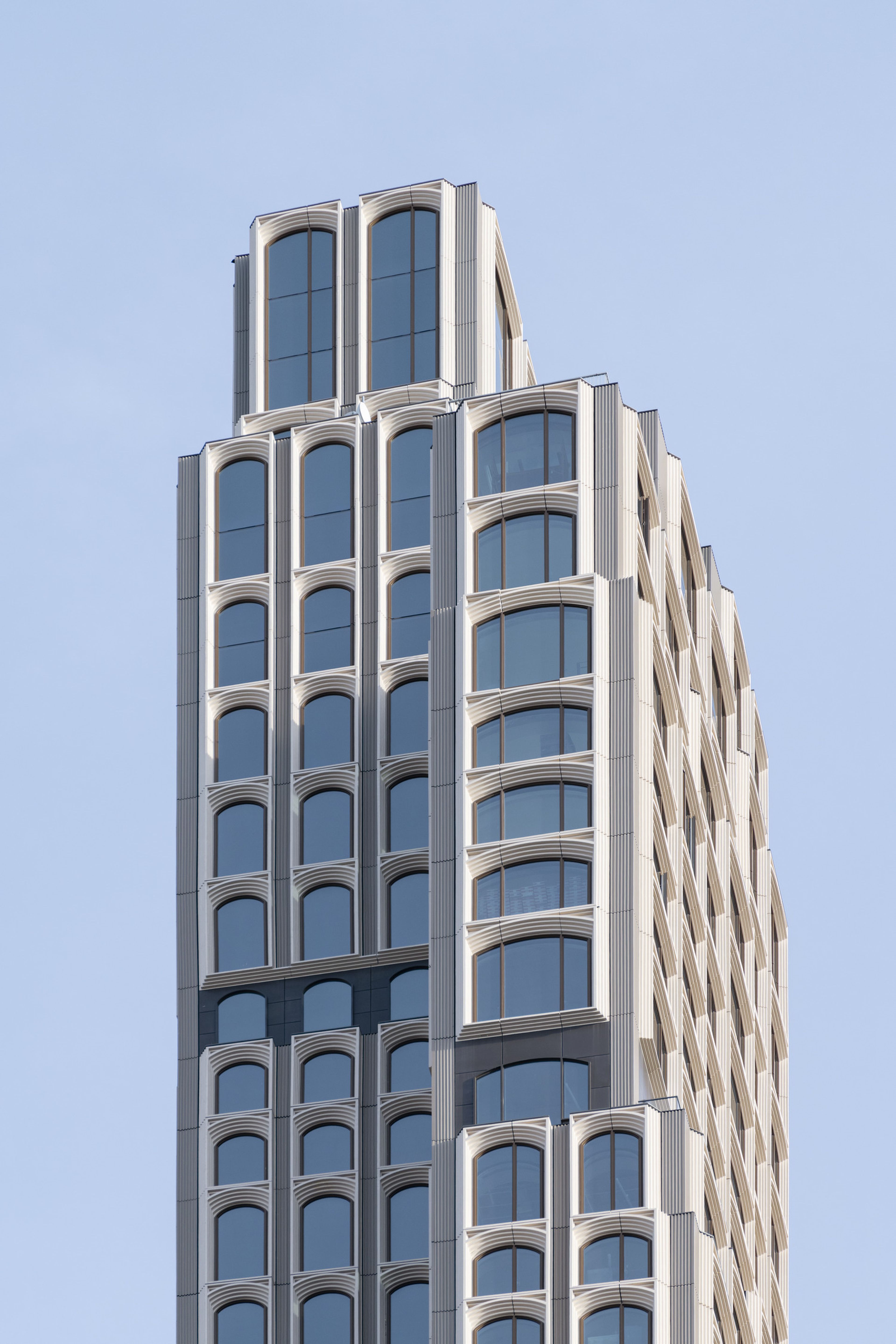 Modern skyscraper with a unique, geometric facade of arched windows and cream-colored accents against a clear blue sky.