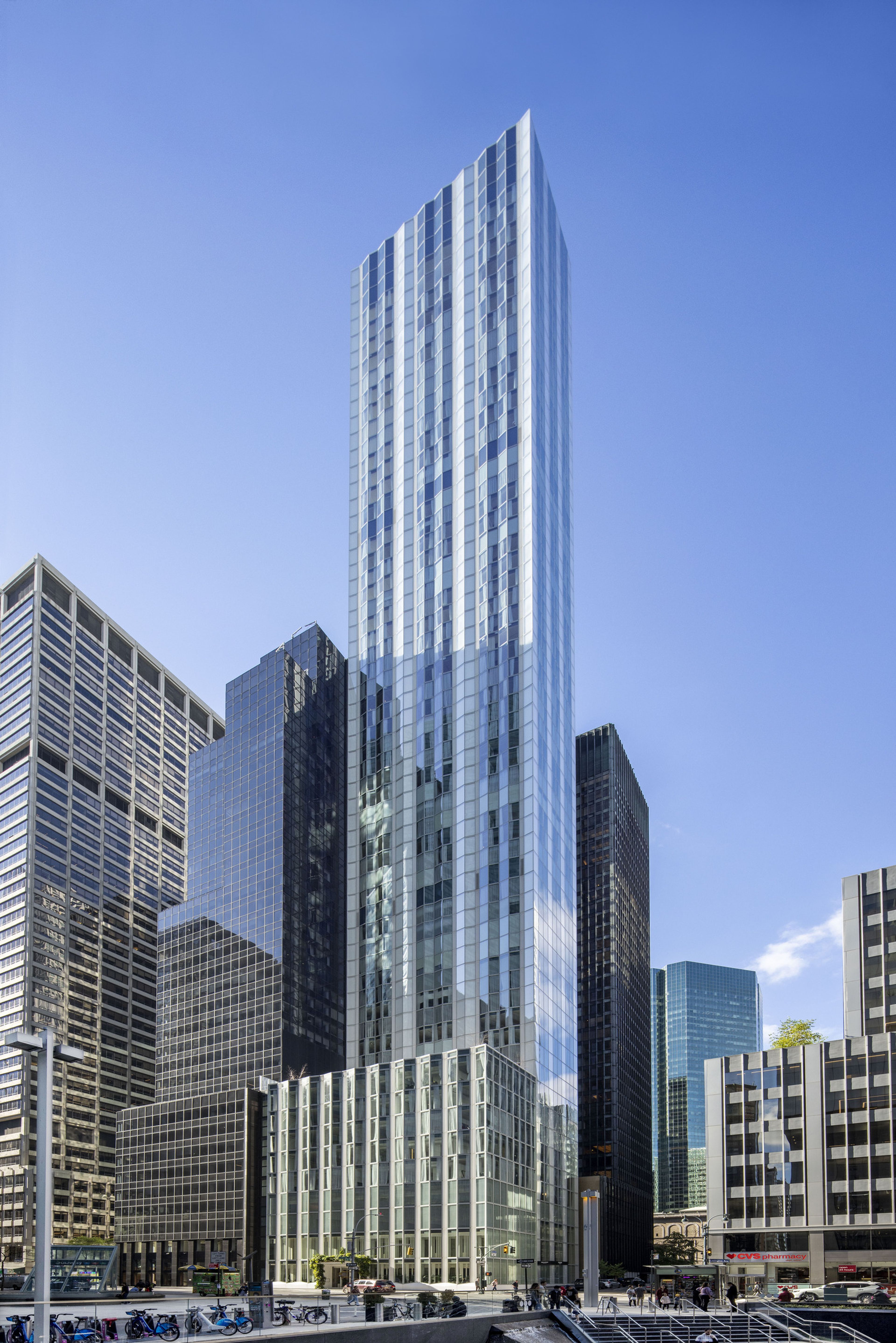 Tall, modern skyscraper with reflective glass facade against a clear blue sky, surrounded by other high-rise buildings.