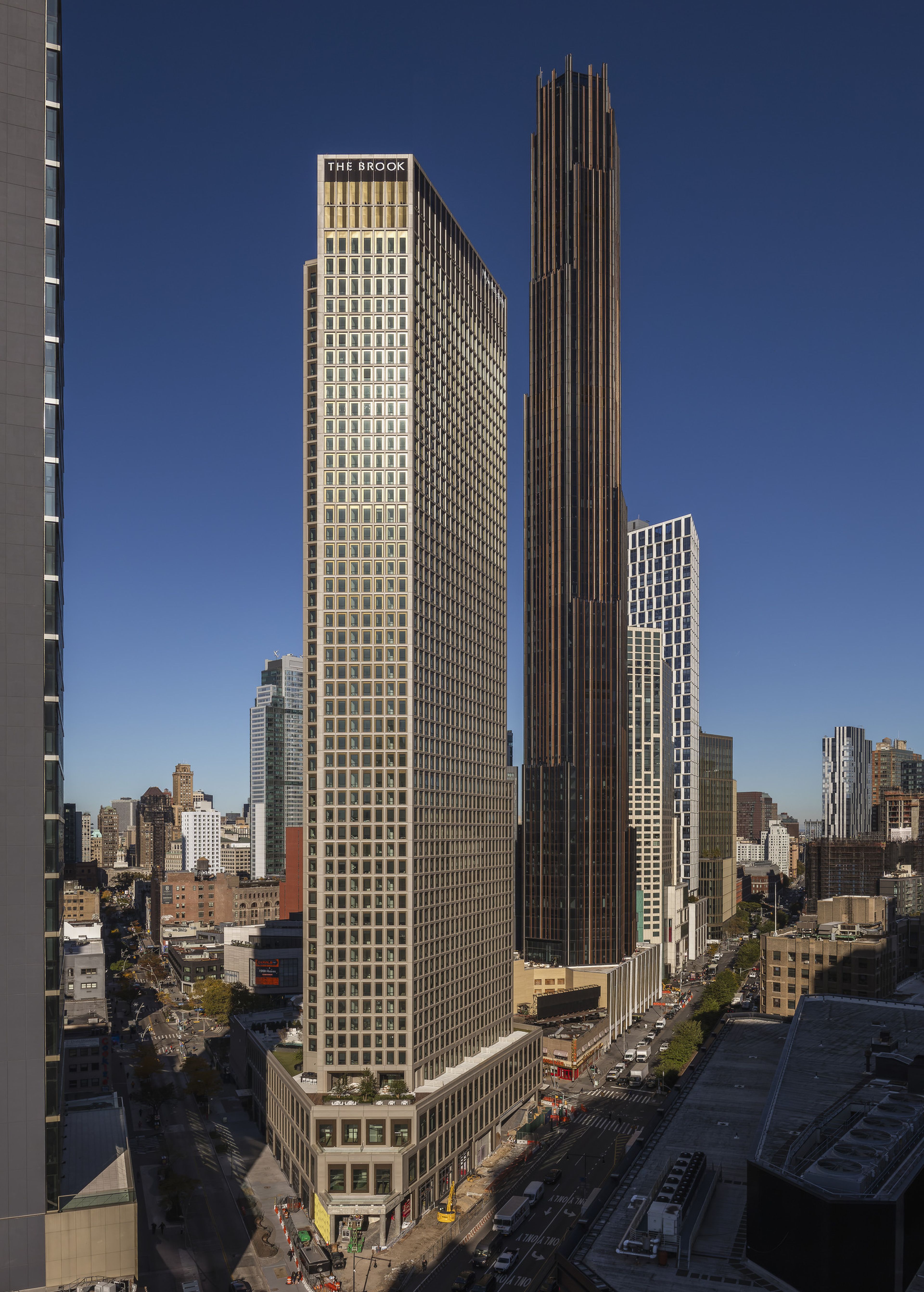 Cityscape with tall buildings under a clear blue sky, featuring "The Brook" prominently. Streets and traffic are visible below.