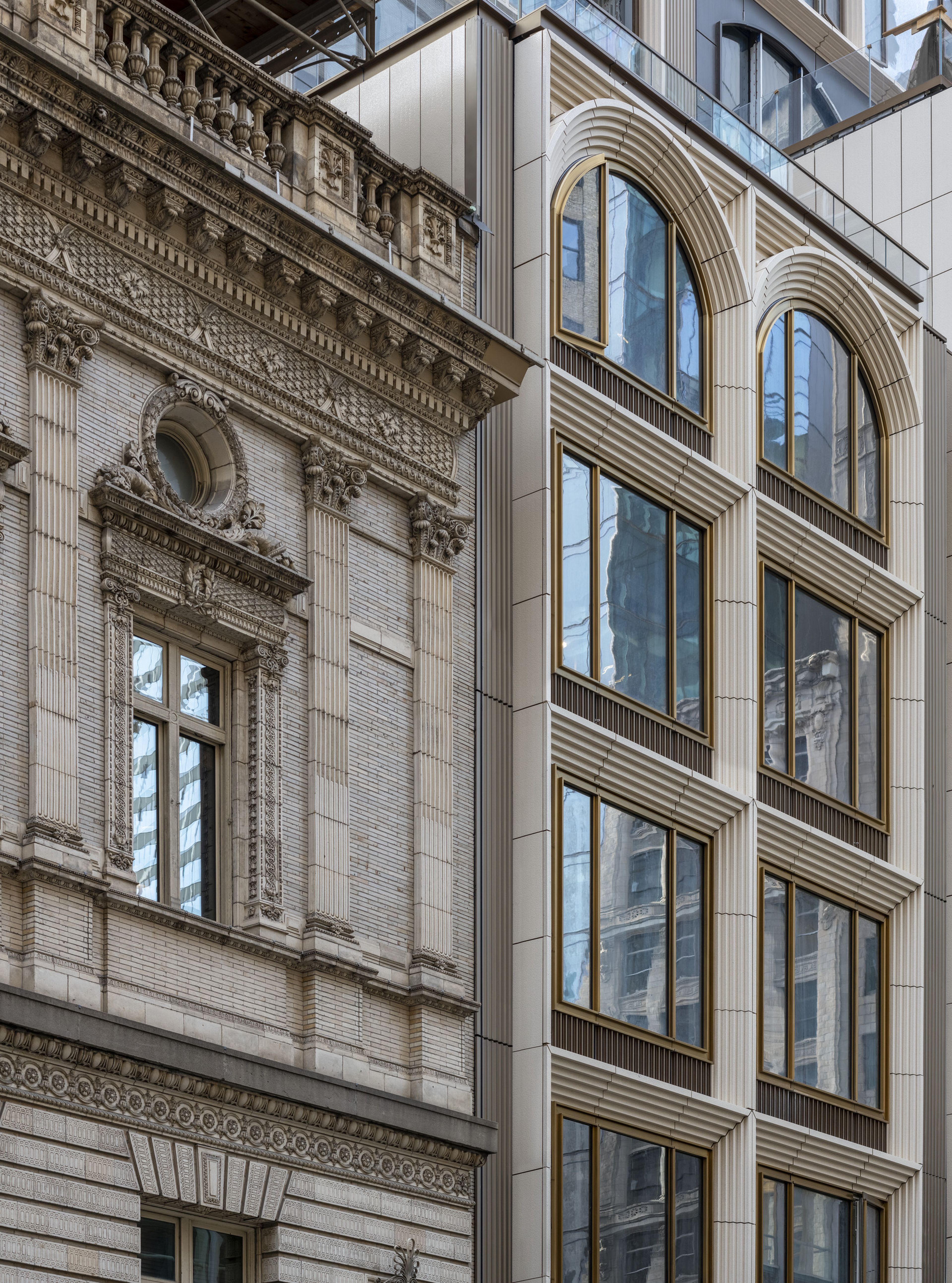 A classical ornate building with intricate stonework next to a modern building with large arched windows and sleek lines.