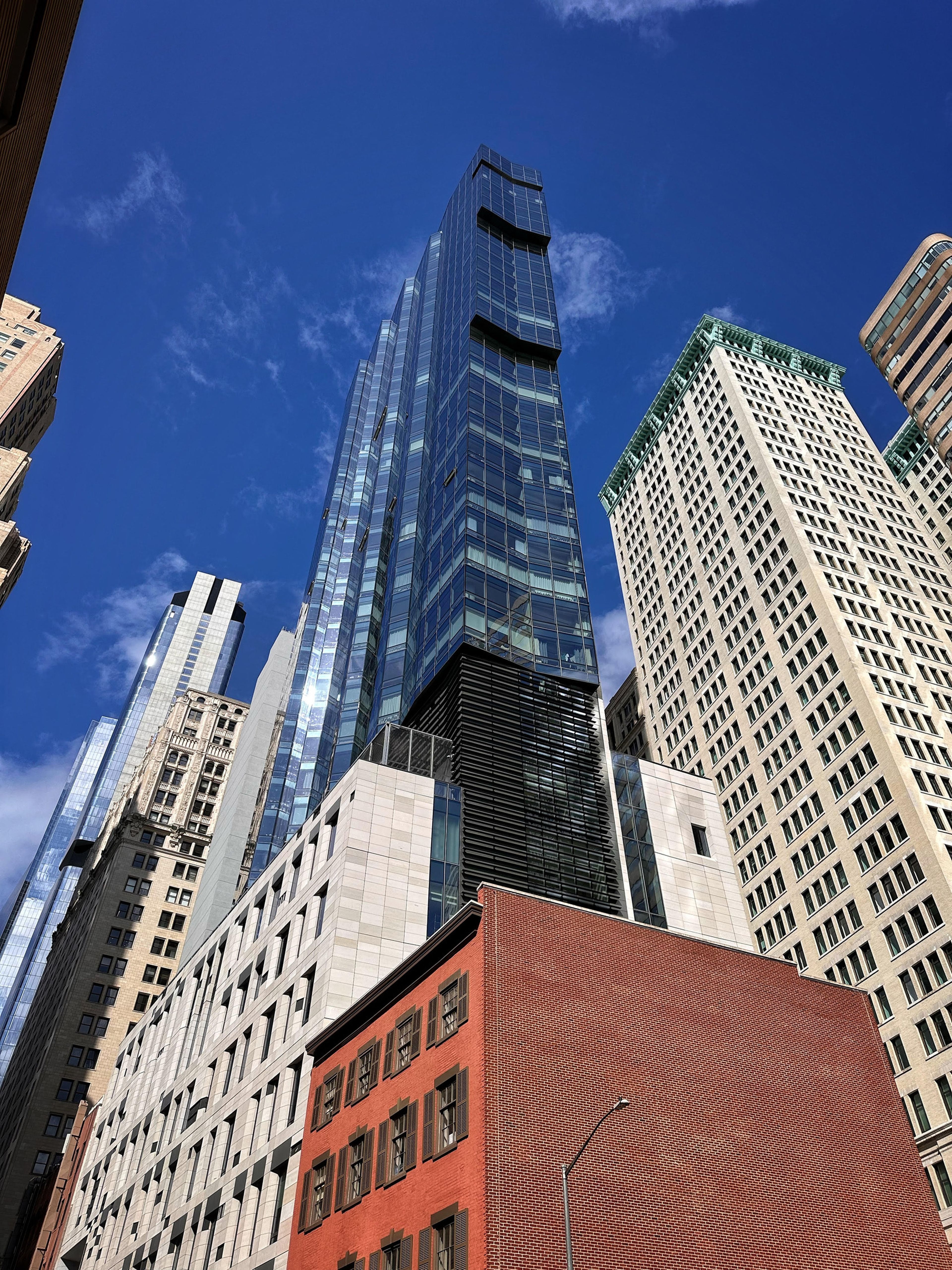 Tall glass skyscraper among other buildings against a blue sky with light clouds.