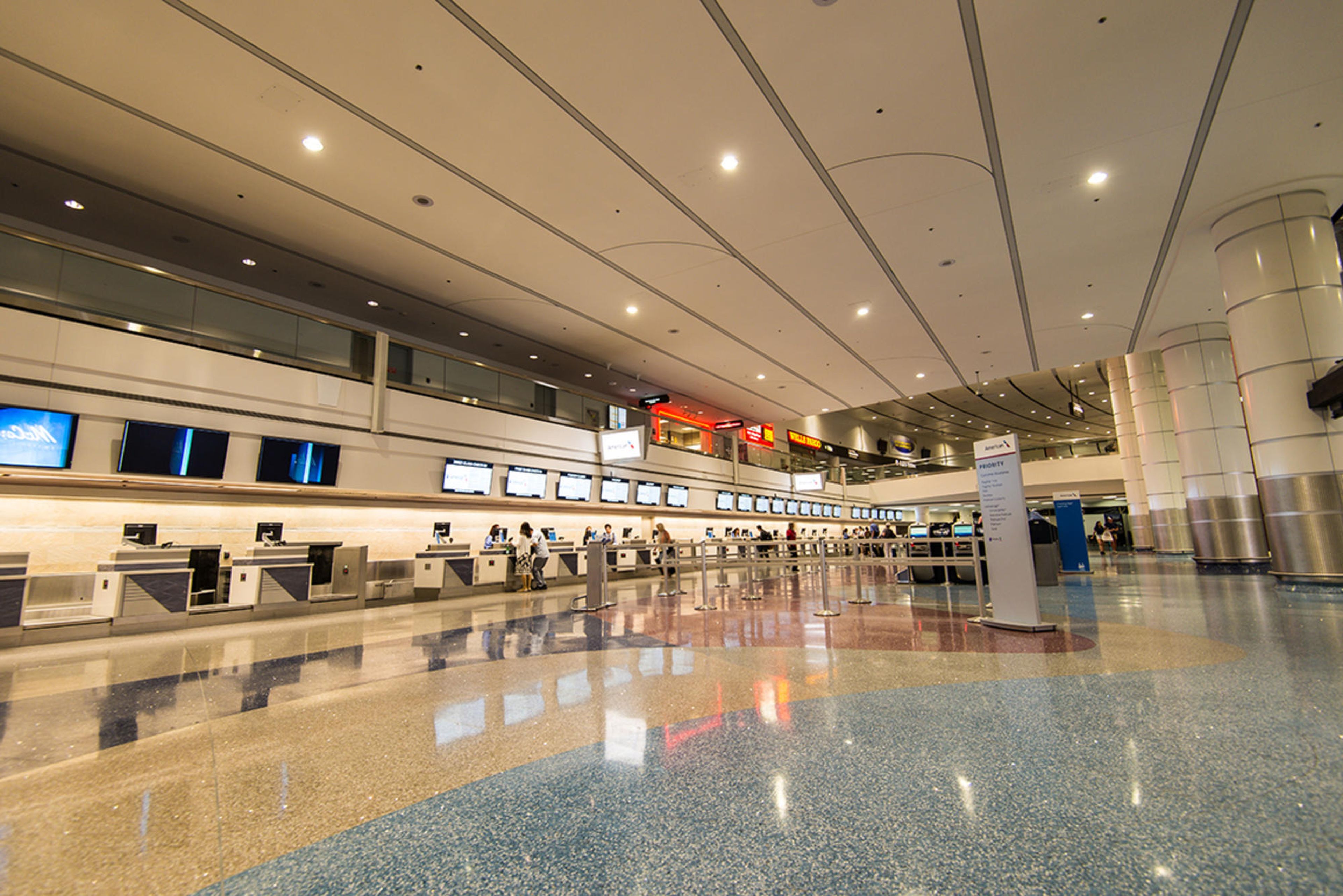 Wide-angle view of an empty airport check-in area with multiple counters, digital screens, and a polished terrazzo floor.