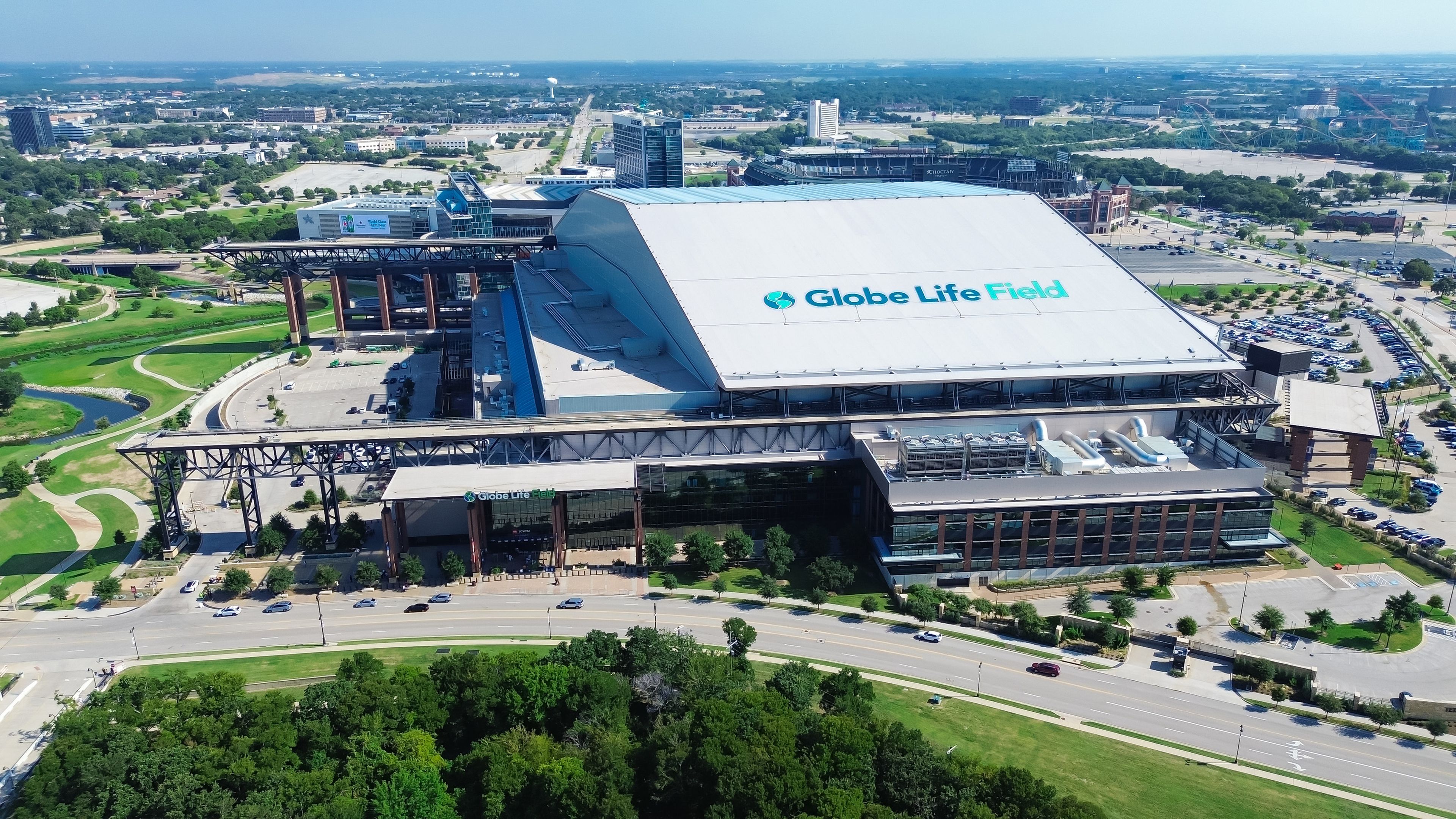 Aerial view of Globe Life Field, a large stadium with a retractable roof, surrounded by roads and greenery in an urban area.