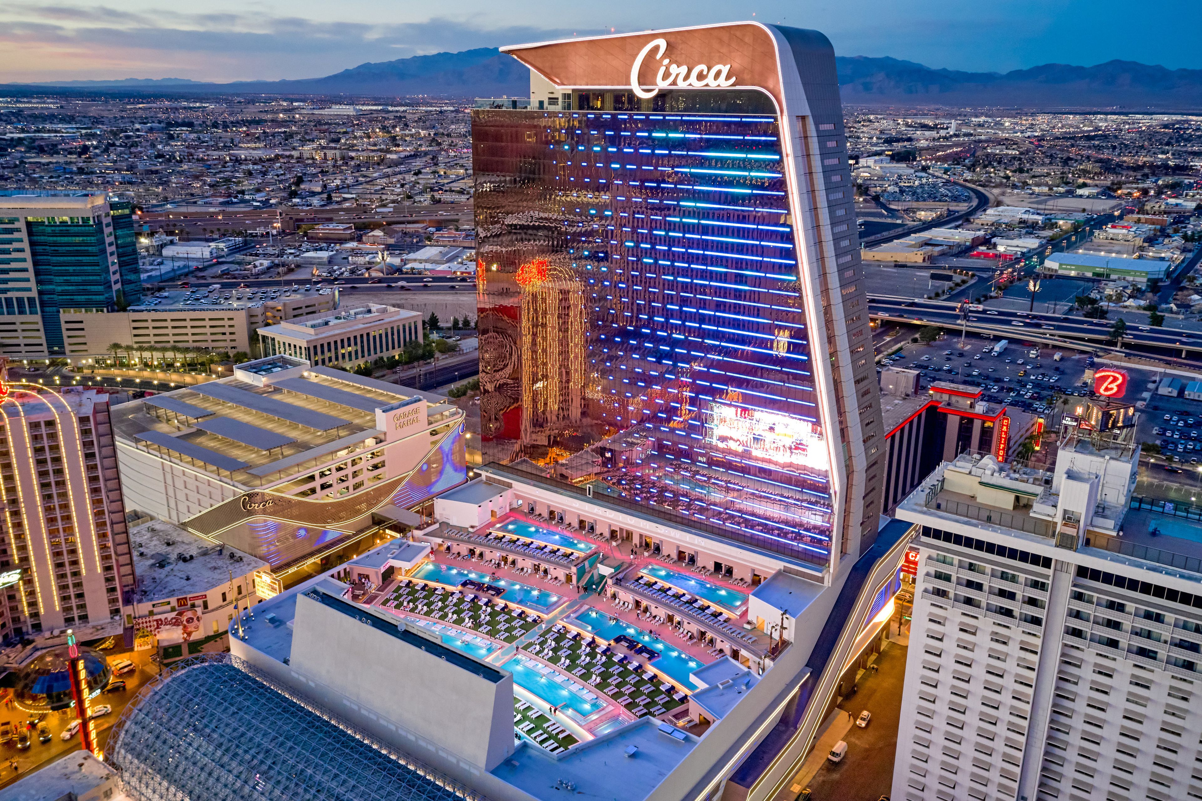 Aerial view of the Circa Resort & Casino in Las Vegas, featuring a rooftop pool, illuminated facade, and surrounding cityscape.
