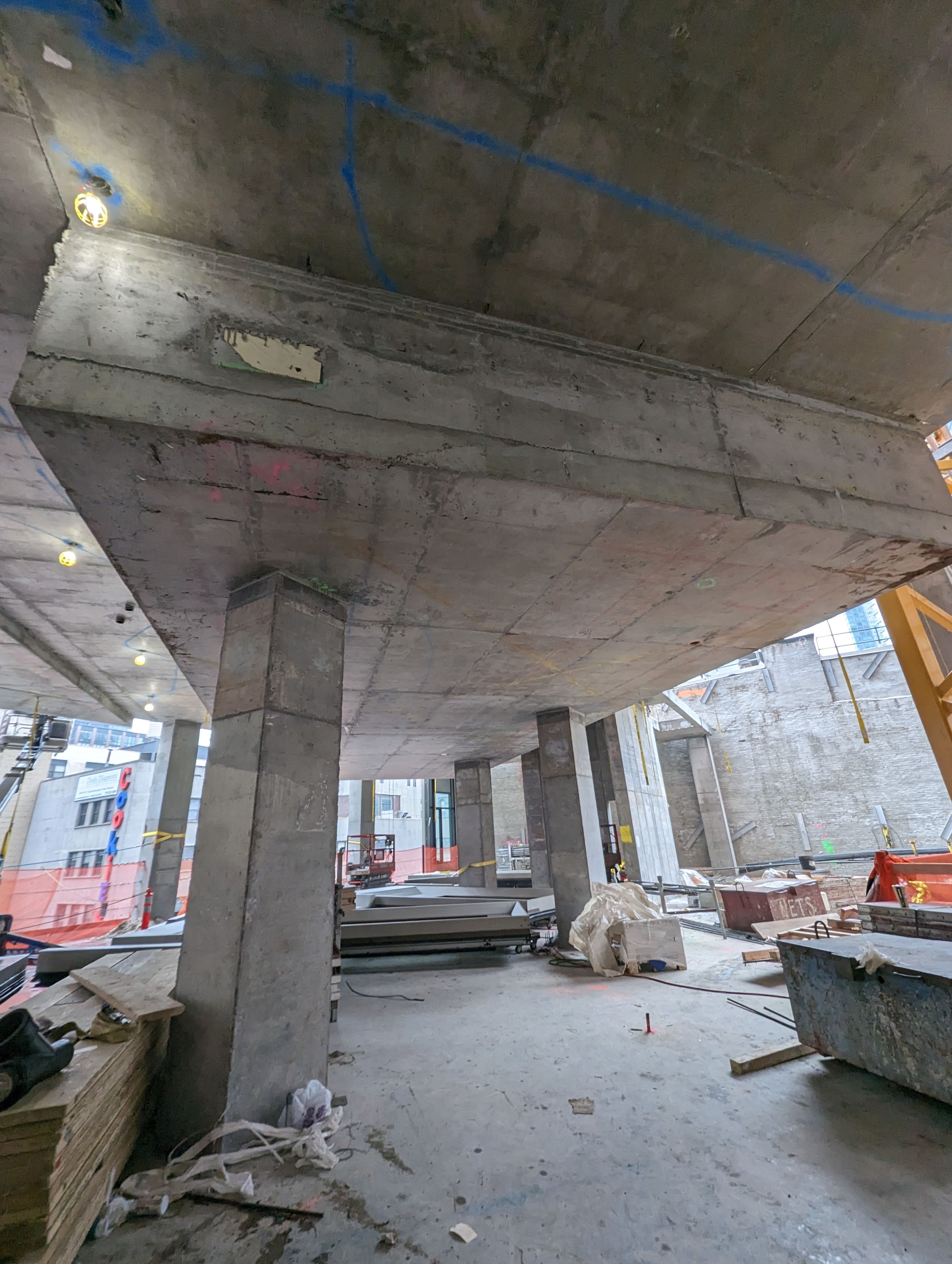 Concrete construction site with pillars, scattered materials, and tools. Overhead lights illuminate the unfinished structure.