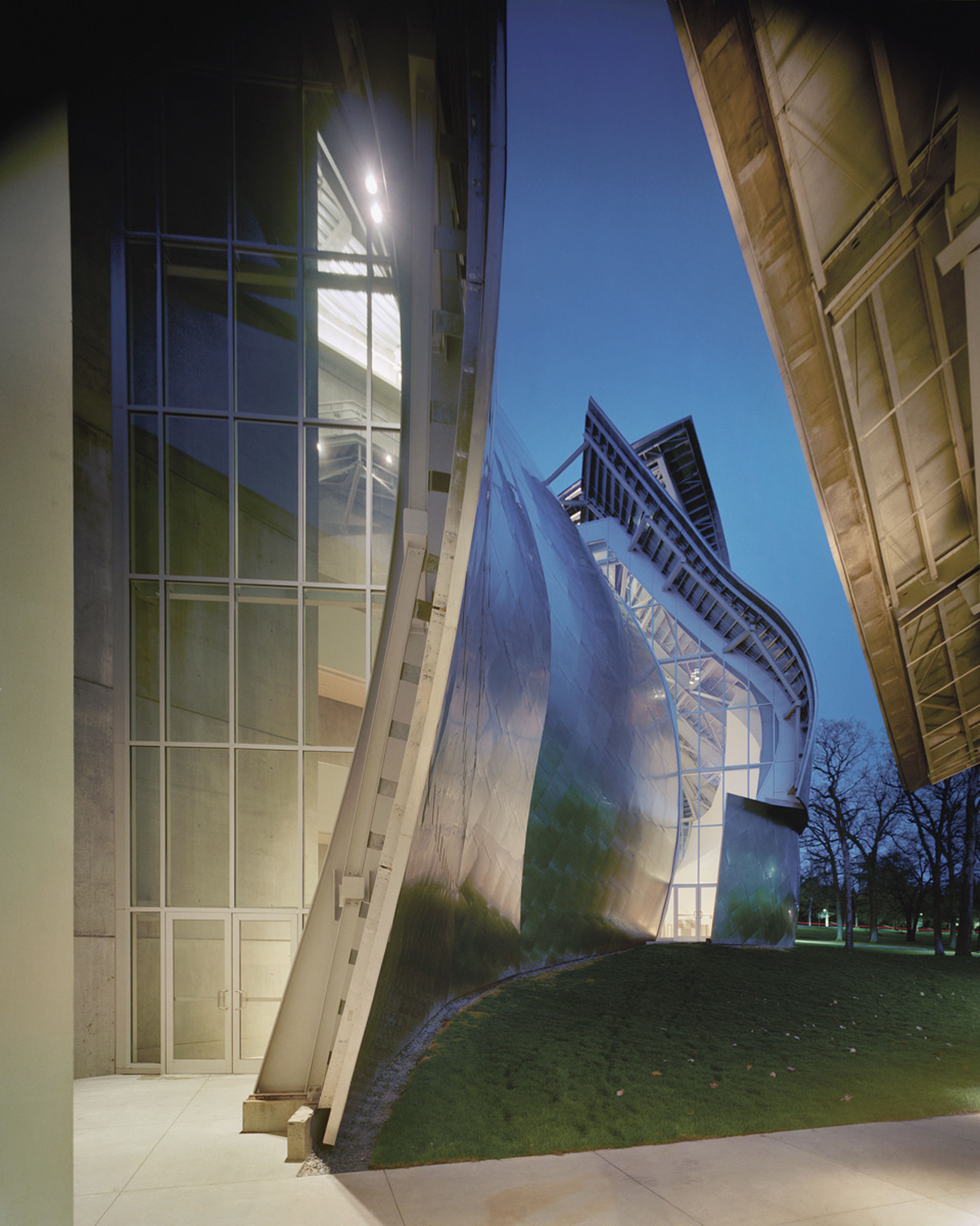 Modern building with curved metal and glass facade, illuminated against a twilight sky.