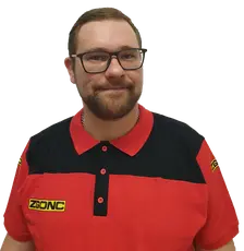 Mann mit Brille und Bart im rot-schwarzen ZGONC-Poloshirt, lächelnd vor weißem Hintergrund.