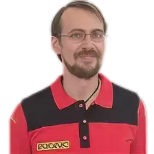Mann mit Brille und Bart trägt rotes und schwarzes Poloshirt mit gelbem Logo, lächelt vor weißem Hintergrund.