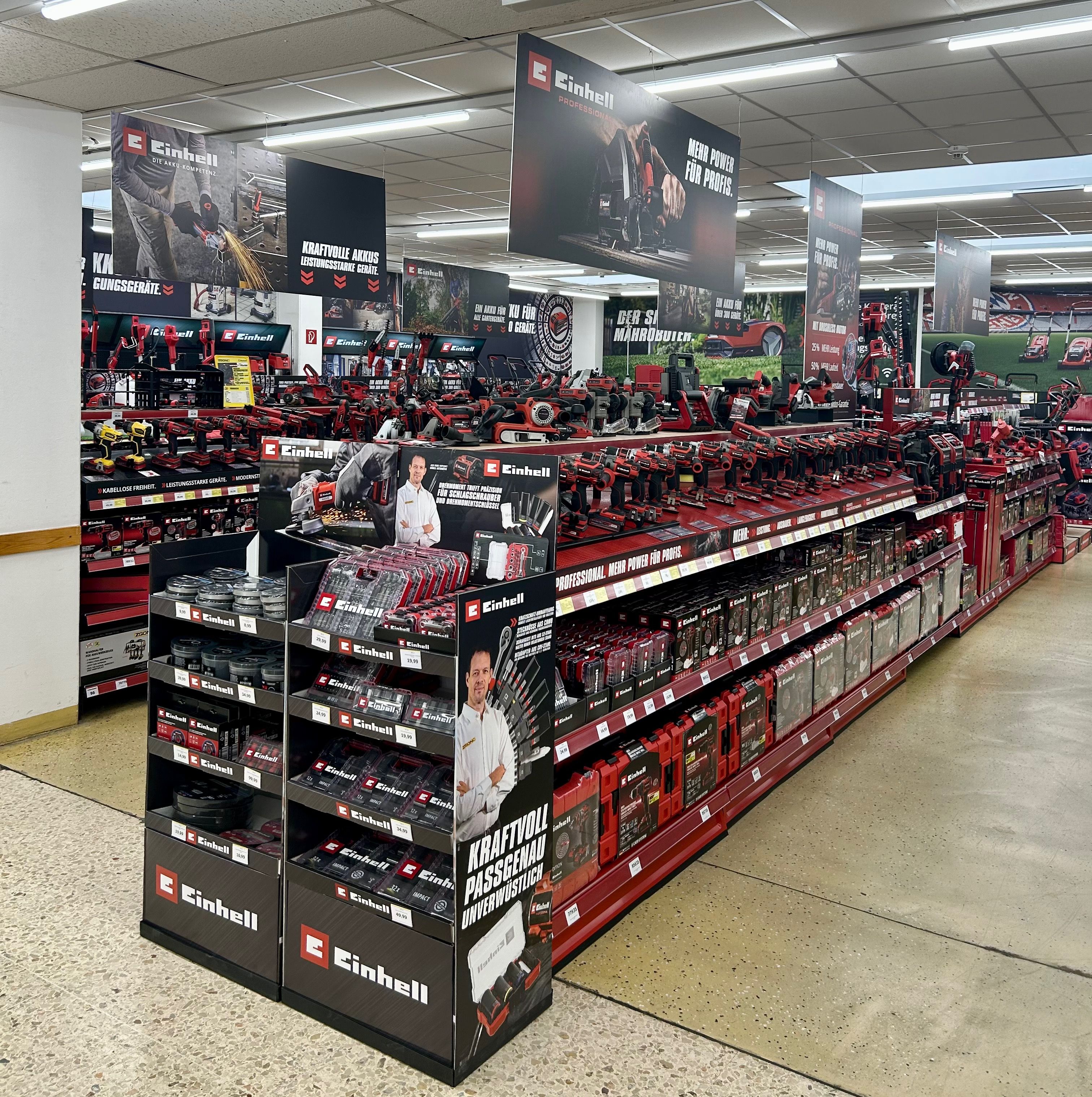 Einhell Markenpräsentation im Baumarkt mit rot-schwarzen Elektrowerkzeugen auf langen Regalen und Werbedisplays.