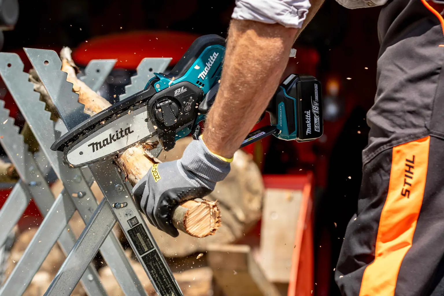 Person sägt mit einer Makita 18V Akku-Kettensäge einen Ast auf einem Sägebock, Holzspäne fliegen umher.