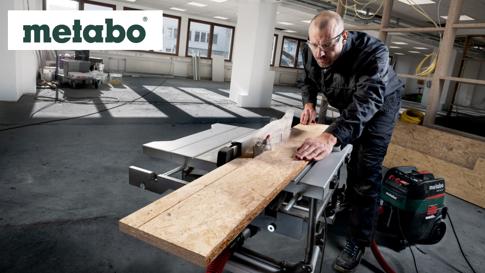 Handwerker mit Schutzbrille sägt Holzplatte auf Metabo-Tischkreissäge auf einer Baustelle.