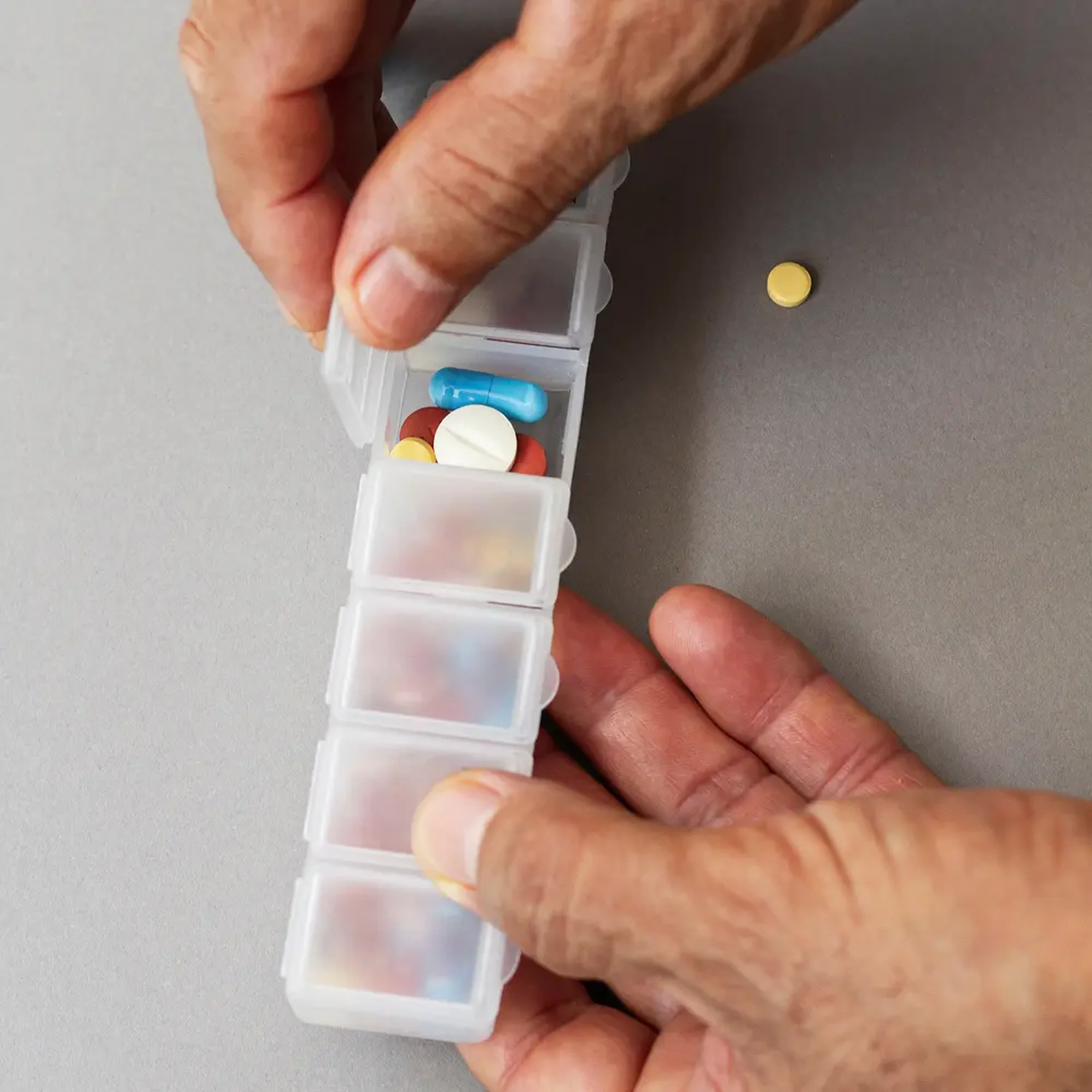 Χέρια ασθενούς οργανώνουν εβδομαδιαίο κουτί φαρμάκων με πολύχρωμα χάπια