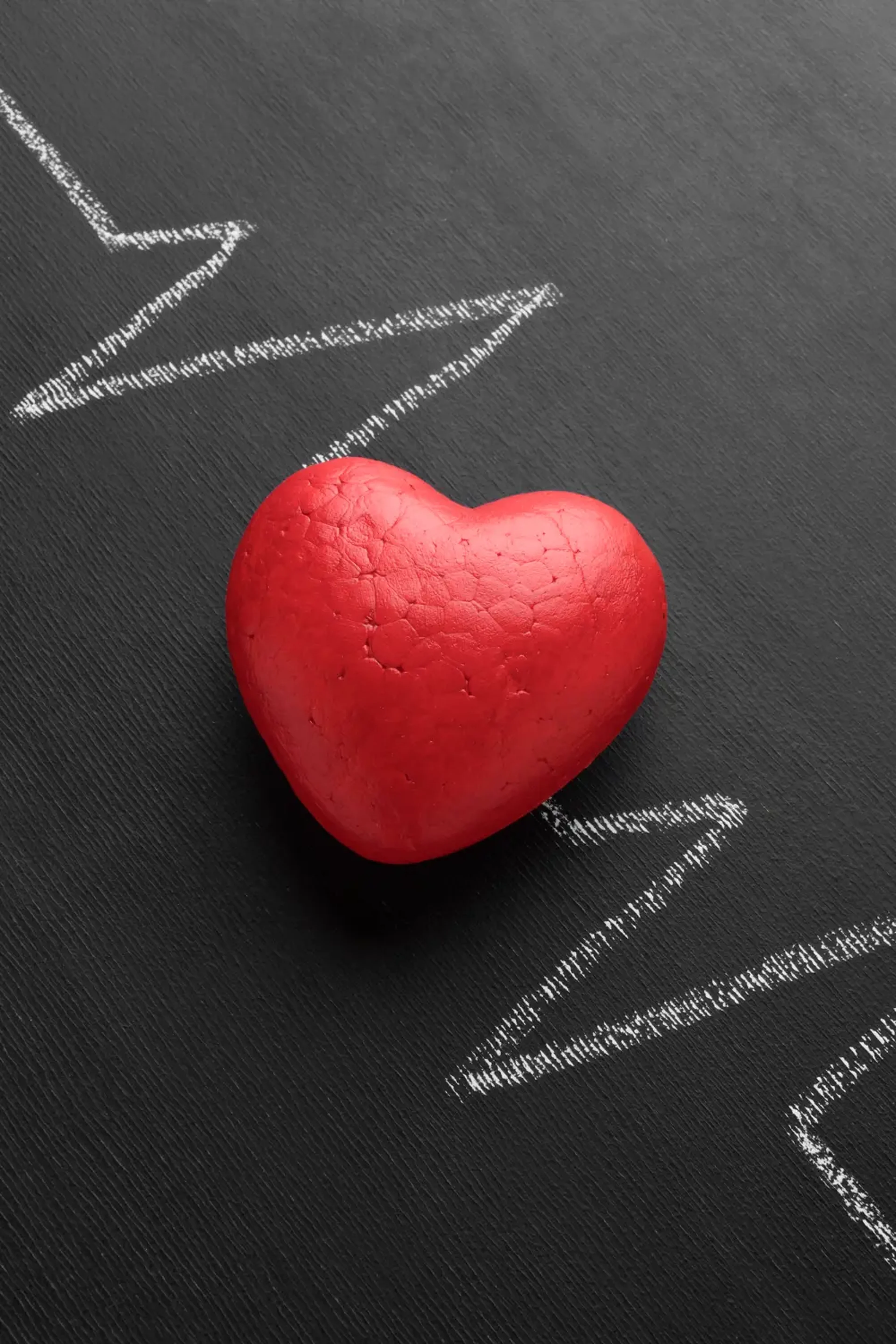 Κόκκινη καρδιά σε σκούρο φόντο με λευκά σχέδια ηλεκτροκαρδιογραφήματος που συμβολίζουν την καρδιαγγειακή υγεία