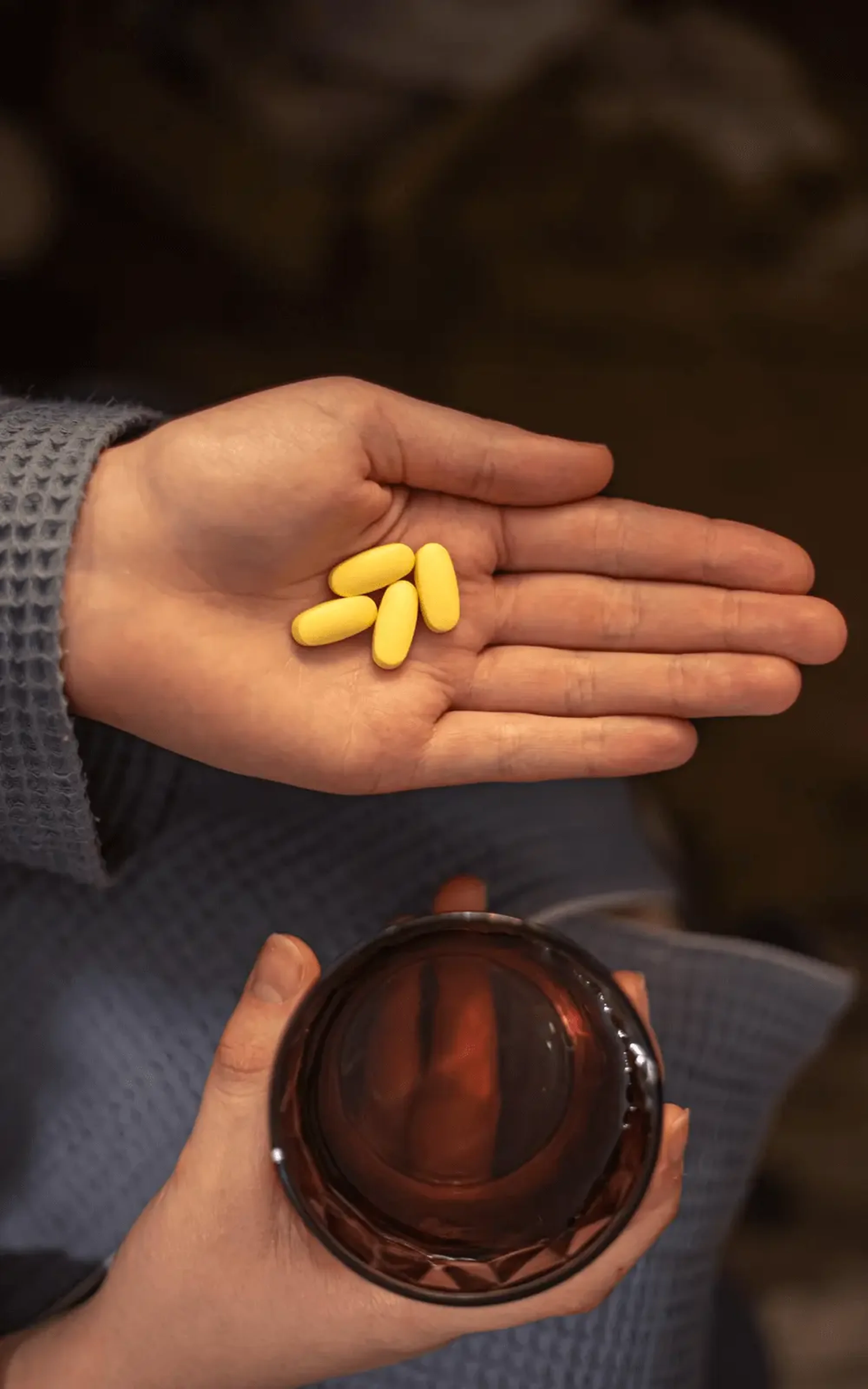 Χέρι που κρατά κίτρινες κάψουλες φαρμάκου με μπουκάλι στο άλλο χέρι