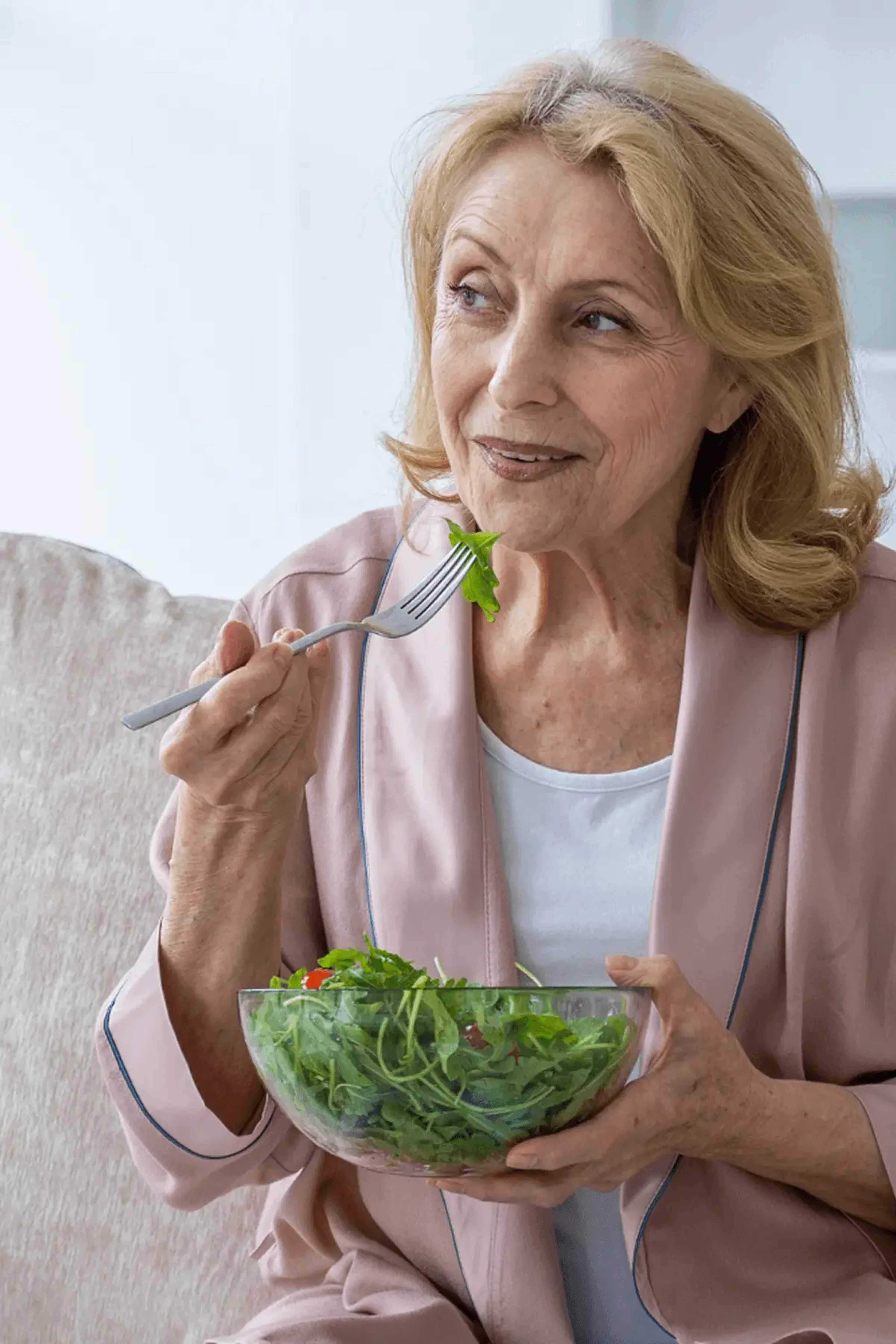 Ηλικιωμένη γυναίκα σε ροζ ζακέτα που τρώει υγιεινή πράσινη σαλάτα