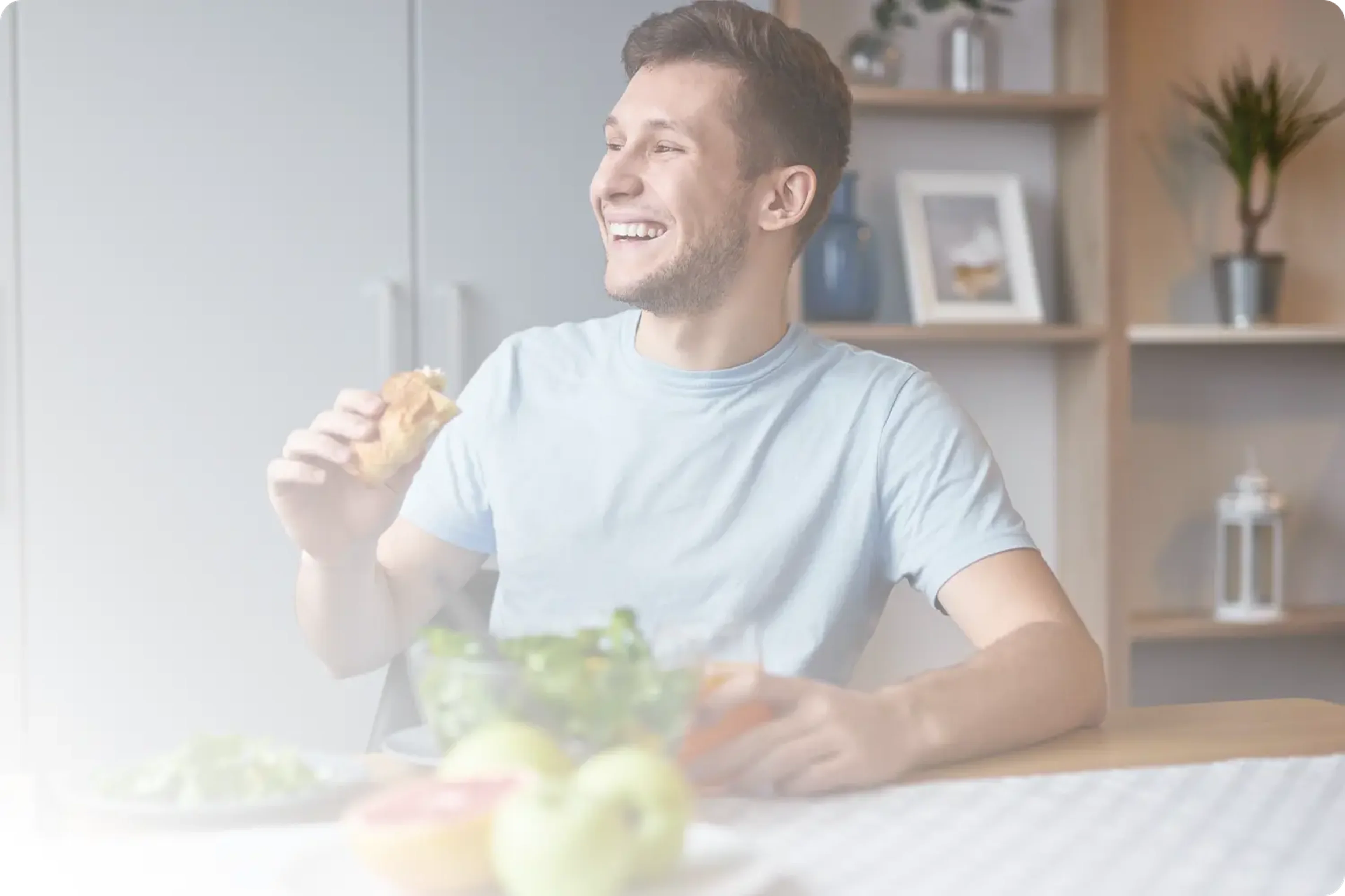 Νεαρός άνδρας σε γαλάζιο μπλουζάκι που τρώει υγιεινό σάντουιτς με σαλάτα στο σπίτι