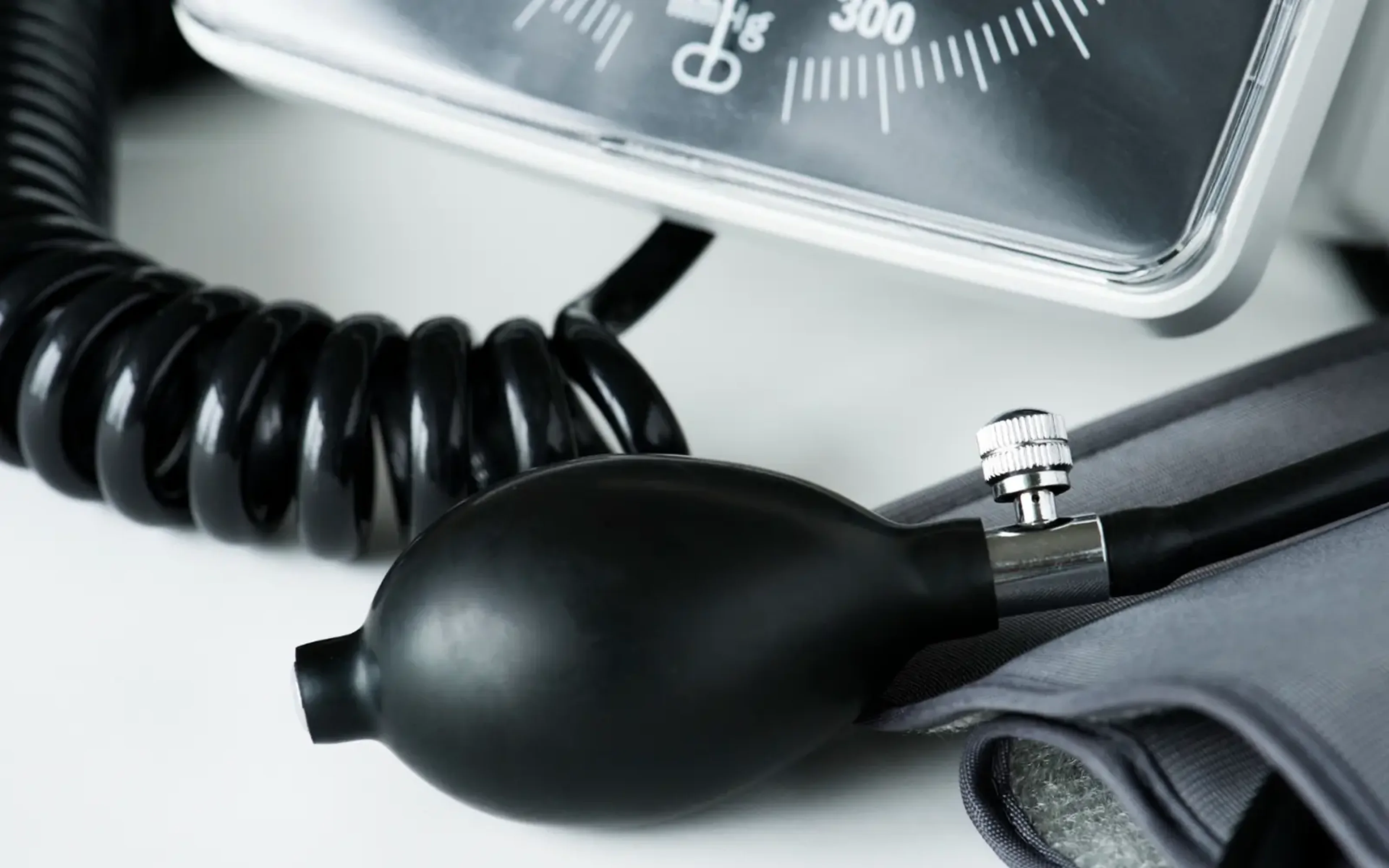 A coiled tube and rubber inflation bulb attached to an analog blood pressure gauge, resting on a white surface.