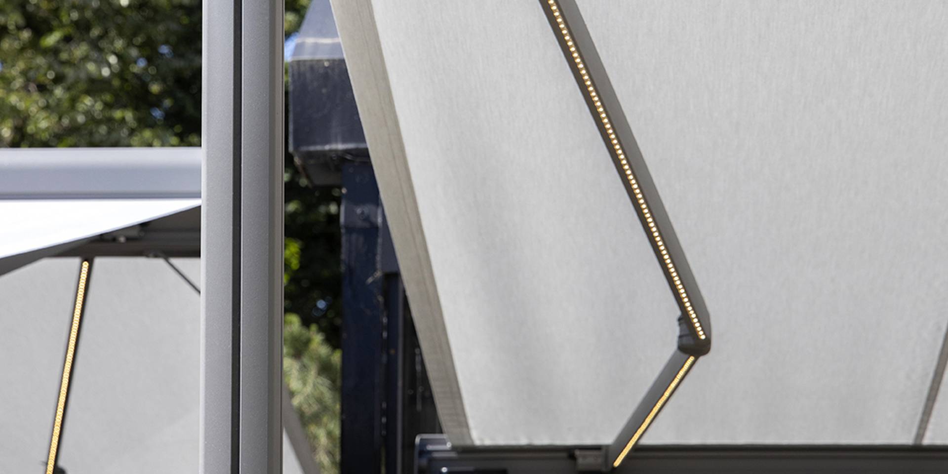 Nahaufnahme eines Brustor‑Sonnenschutzes mit warmweißer LED‑Beleuchtung in den Gelenkarmen, die das hochwertige Tuch und das moderne Design betont.