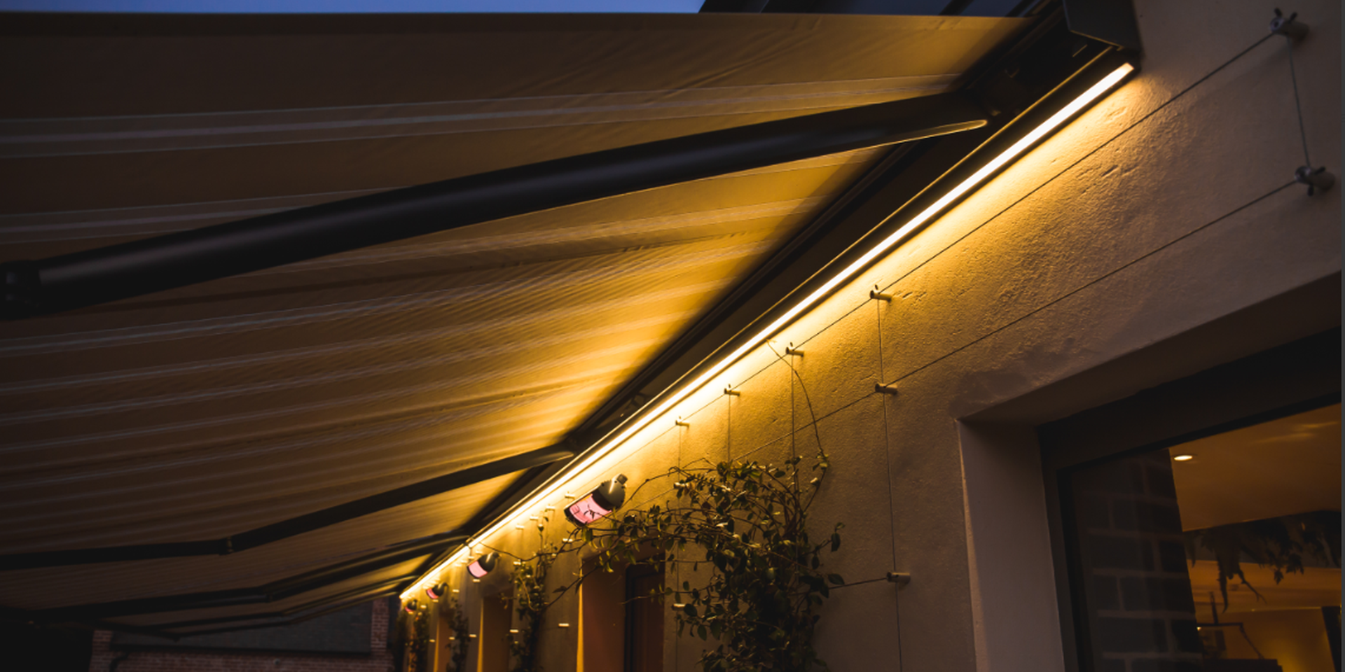 Close‑up of an aluminium awning with integrated warm LED lighting mounted on a house façade during the evening.