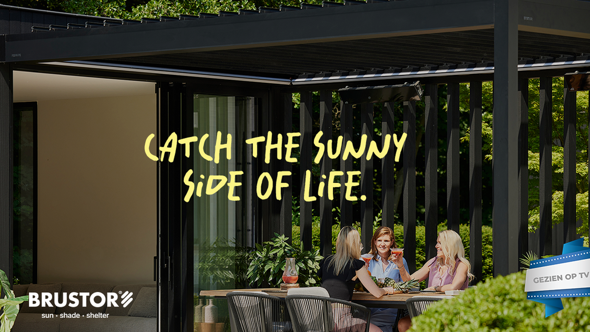 Terrasoverkapping met lamellen waar vier personen aan een buitentafel zitten onder een moderne aluminium pergola van Brustor, omringd door groen.