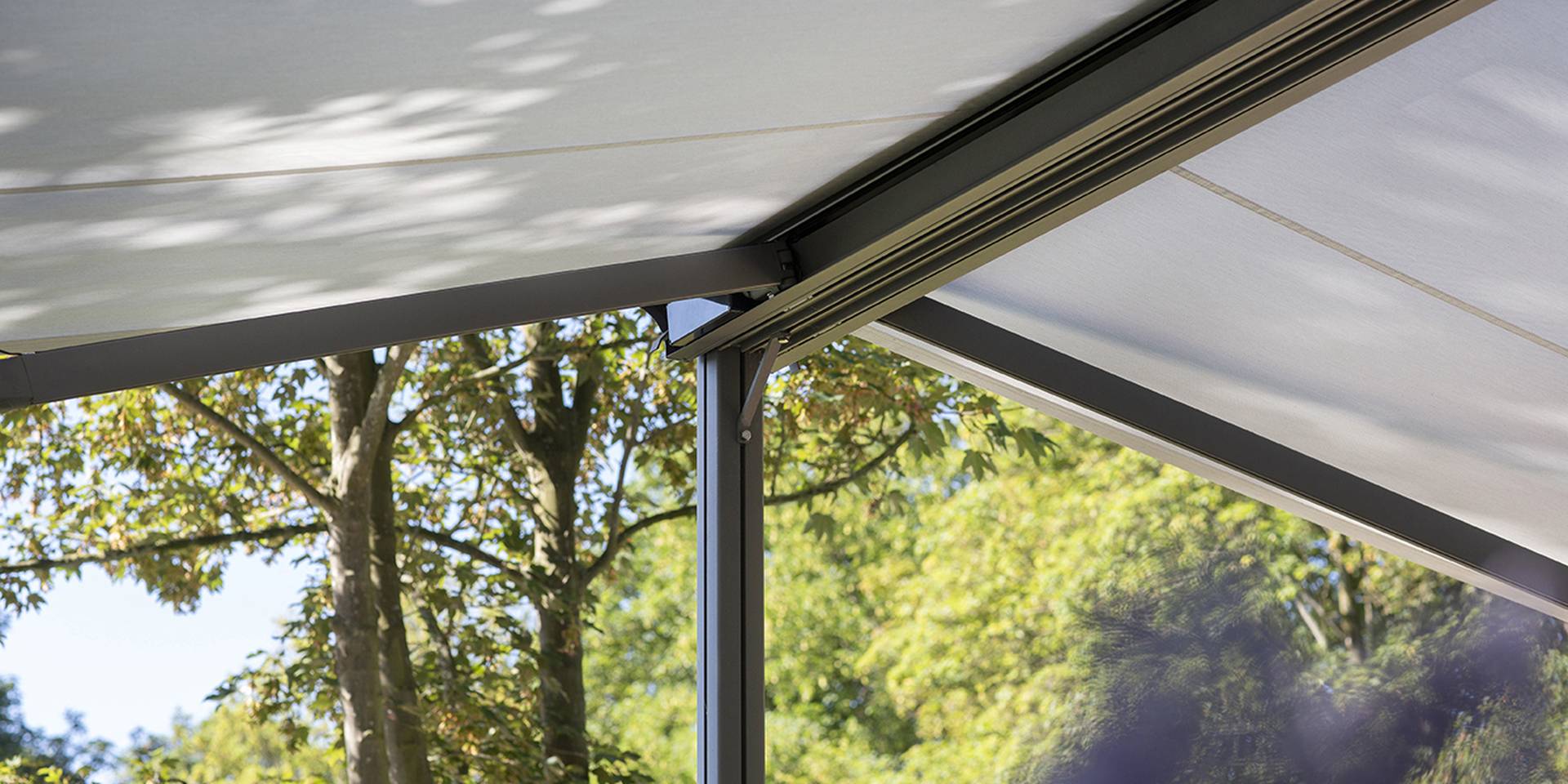 Nahaufnahme eines freistehenden Brustor‑Sonnenschutzsystems mit straff gespanntem Tuch, eingebettet in eine grüne Außenumgebung mit natürlichem Licht.