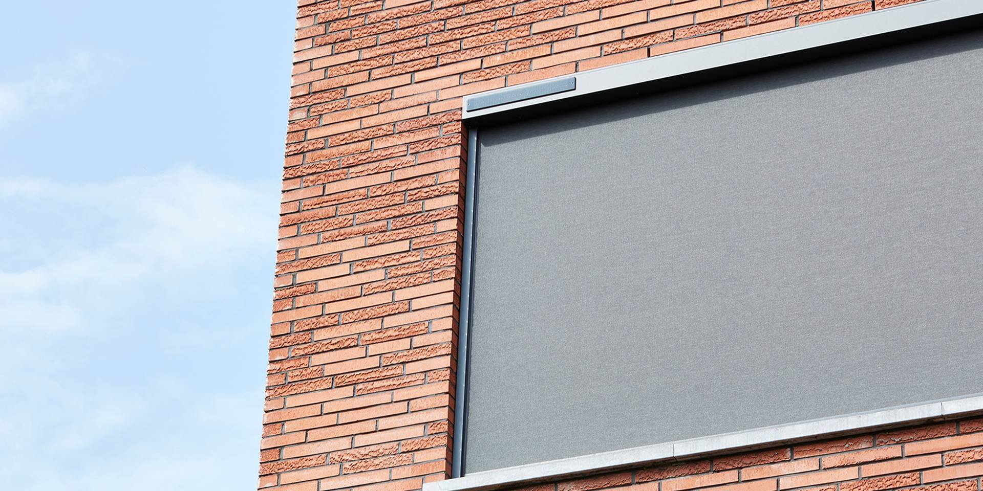 Aluminium ZIP‑screen voor een raam aan een bakstenen gevel, voor strakke en efficiënte buitenzonwering.