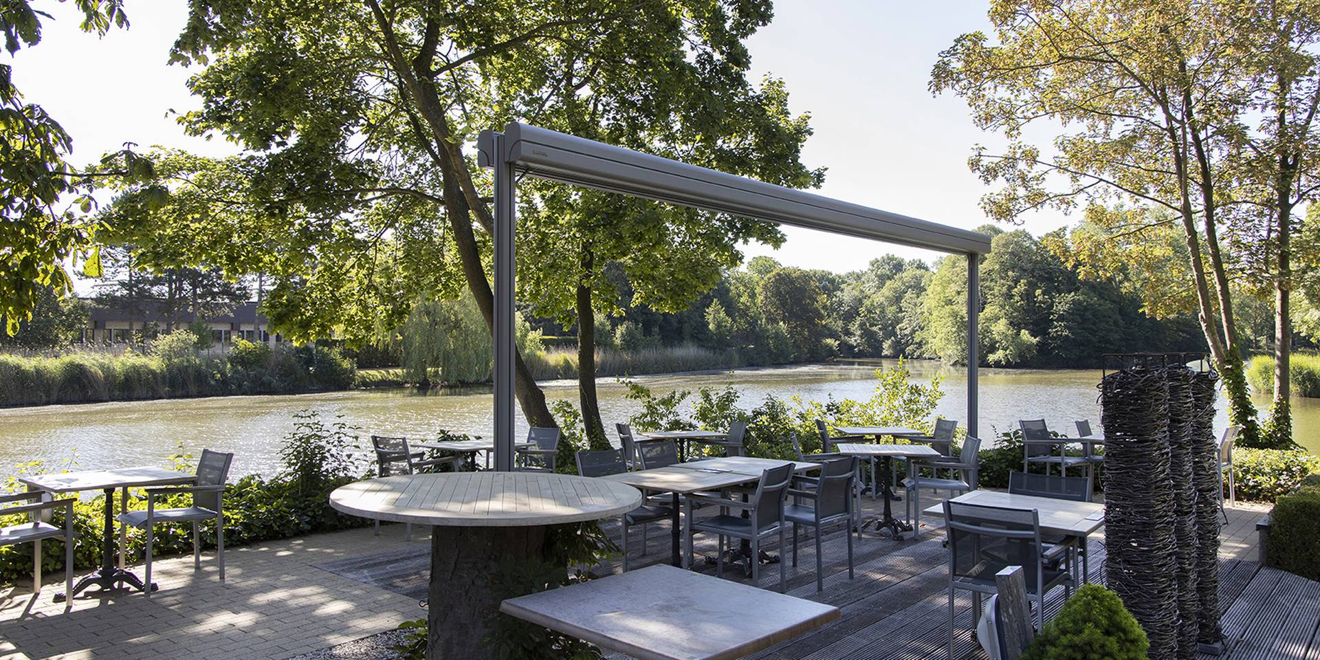 Terrasse am Wasser mit der freistehenden Brustor‑Twinstor‑Sonnenschutzlösung, die angenehmen Schatten und ein naturnahes Außenambiente schafft.