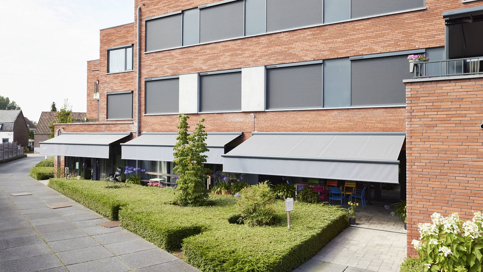Appartementengebouw met aluminium ZIP‑screens en zonneschermen op bakstenen gevels, die buitenzonwering bieden voor ramen en terrassen.