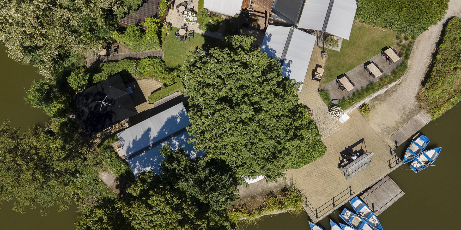 Luftaufnahme der Terrasse am Wasser des Pacific Eiland mit der freistehenden Brustor‑Twinstor‑Sonnenschutzlösung, eingebettet in eine grüne, ruhige Umgebung.